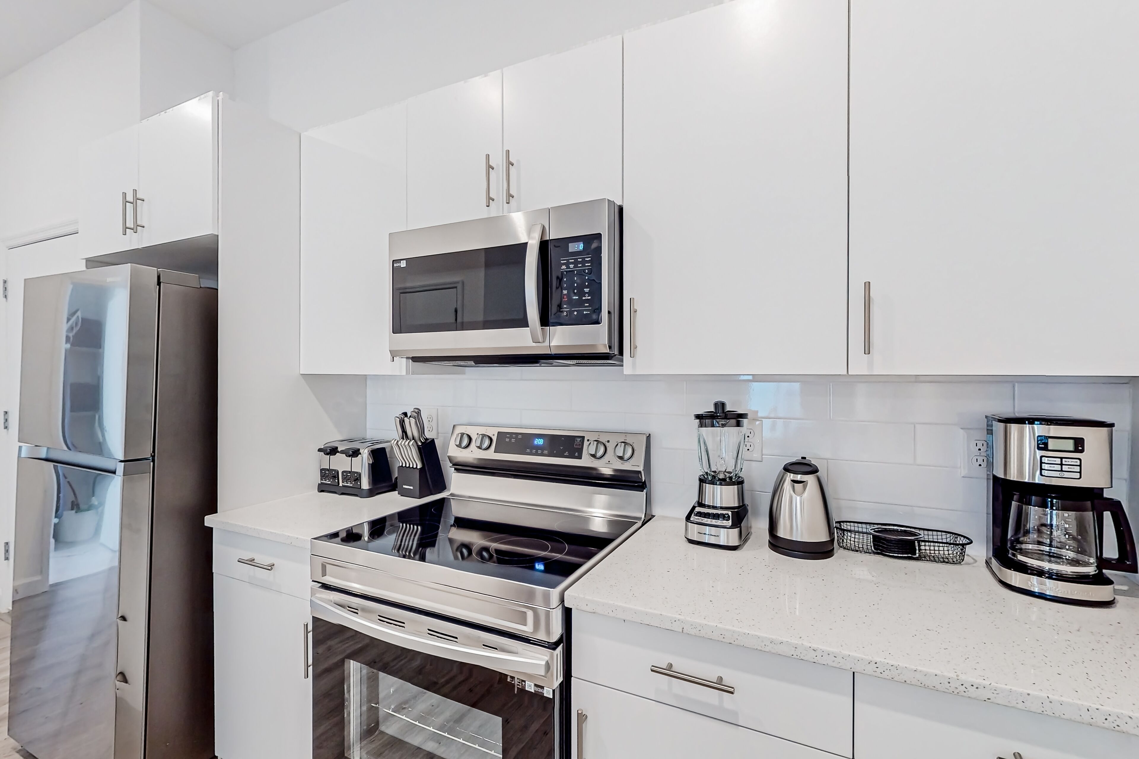 A modern kitchen with stainless steel appliances, white cabinetry, and a countertop with a coffee maker and toaster.