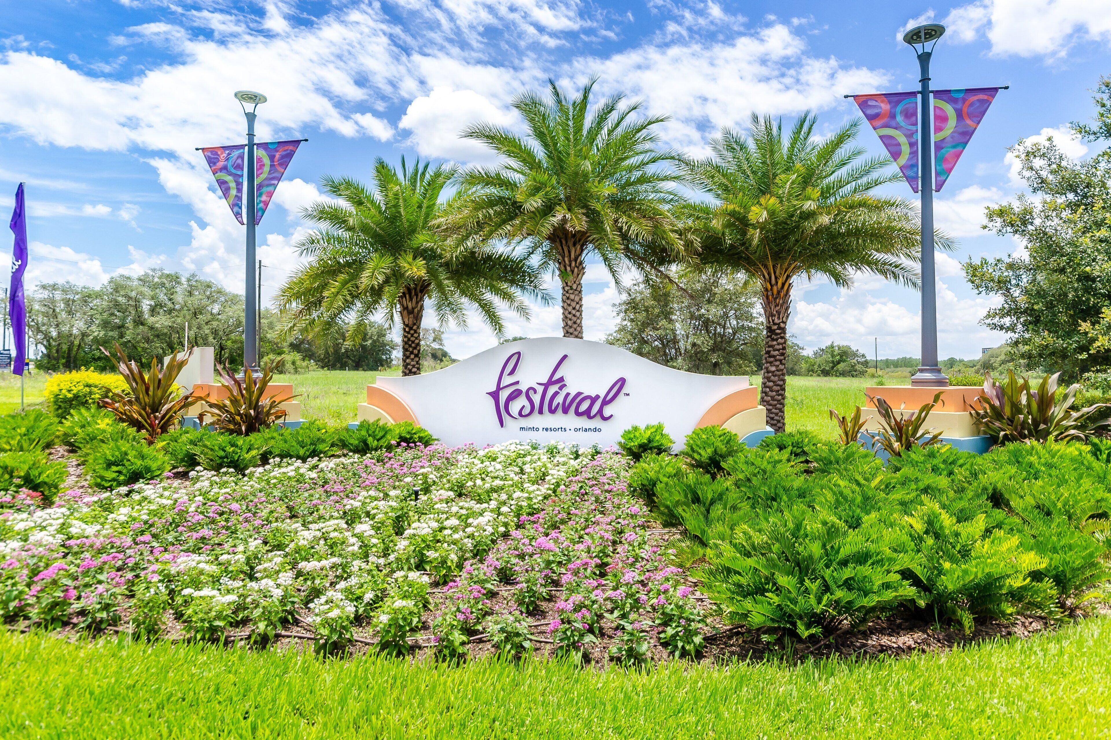 A sign with 'festival' written on it, surrounded by palm trees and a flower garden.