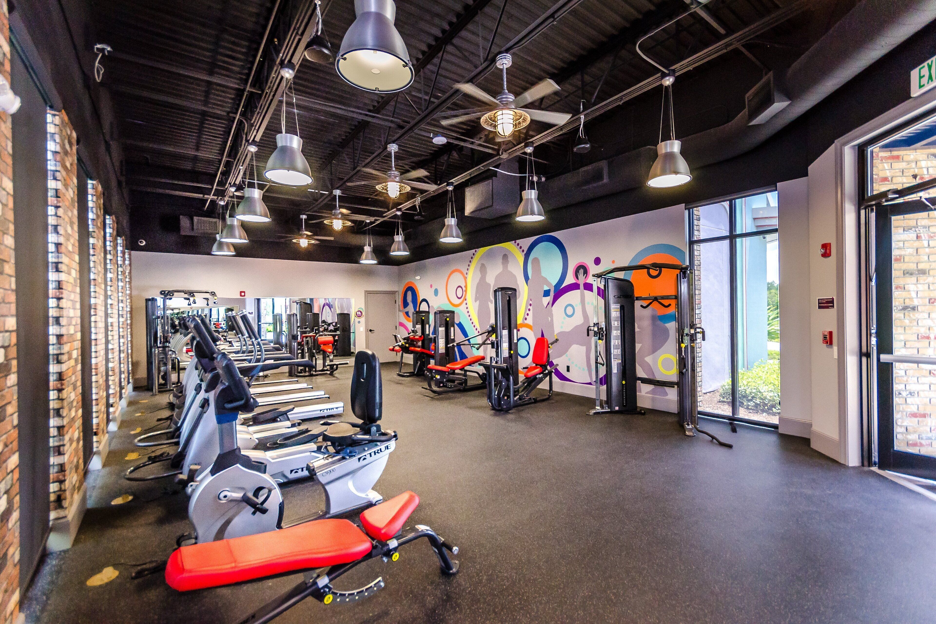 A gym with exercise equipment, a mural, and large windows.