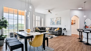 Un salon moderne avec un coin repas, de grandes fenêtres et un ventilateur de plafond.
