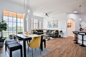 Ein modernes Wohnzimmer mit Essbereich, großen Fenstern und einem Deckenventilator.