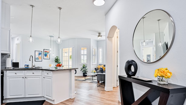 Une cuisine moderne avec des meubles blancs, un îlot central, des luminaires suspendus et un grand miroir.