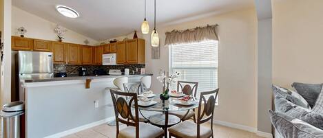 Una cocina moderna con armarios de madera, un refrigerador de acero inoxidable y un comedor con mesa y sillas de vidrio.
