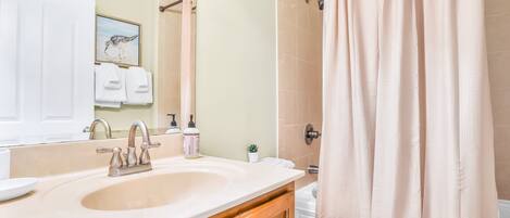 A bathroom with a sink, mirror, towel rack, shower curtain, and a small potted plant.