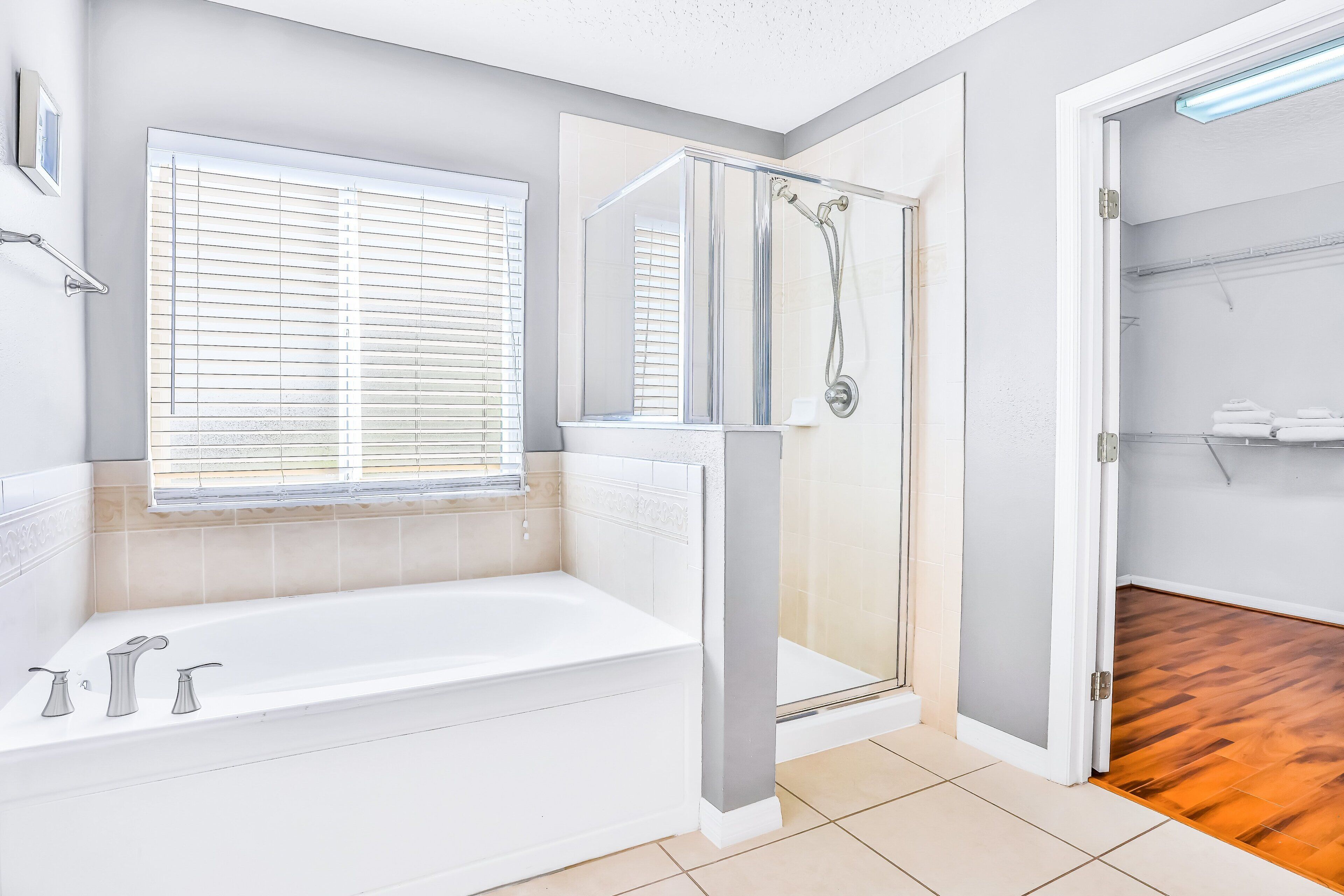 A bathroom with a bathtub, shower, and a window with blinds.
