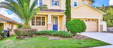 A two-story house with a garage, a well-maintained lawn, and a tall tree.