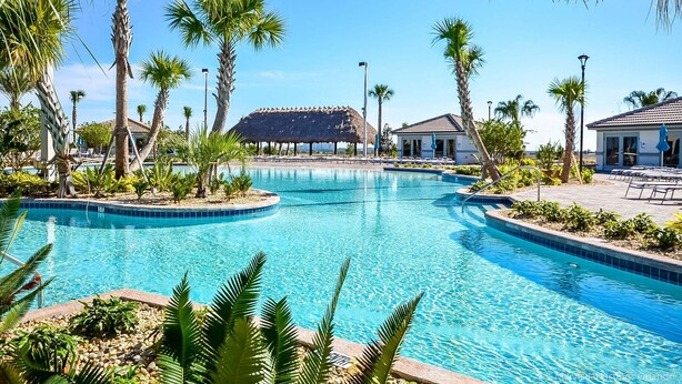 A clear blue pool surrounded by palm trees and a thatched-roof structure. - Family Home Boasting Entertainment for Everyone With Wifi (Davenport)