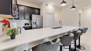 A modern kitchen with dark cabinets, a stainless steel refrigerator, a white countertop, and bar stools. - Family Home Boasting Entertainment for Everyone With Wifi (Davenport)