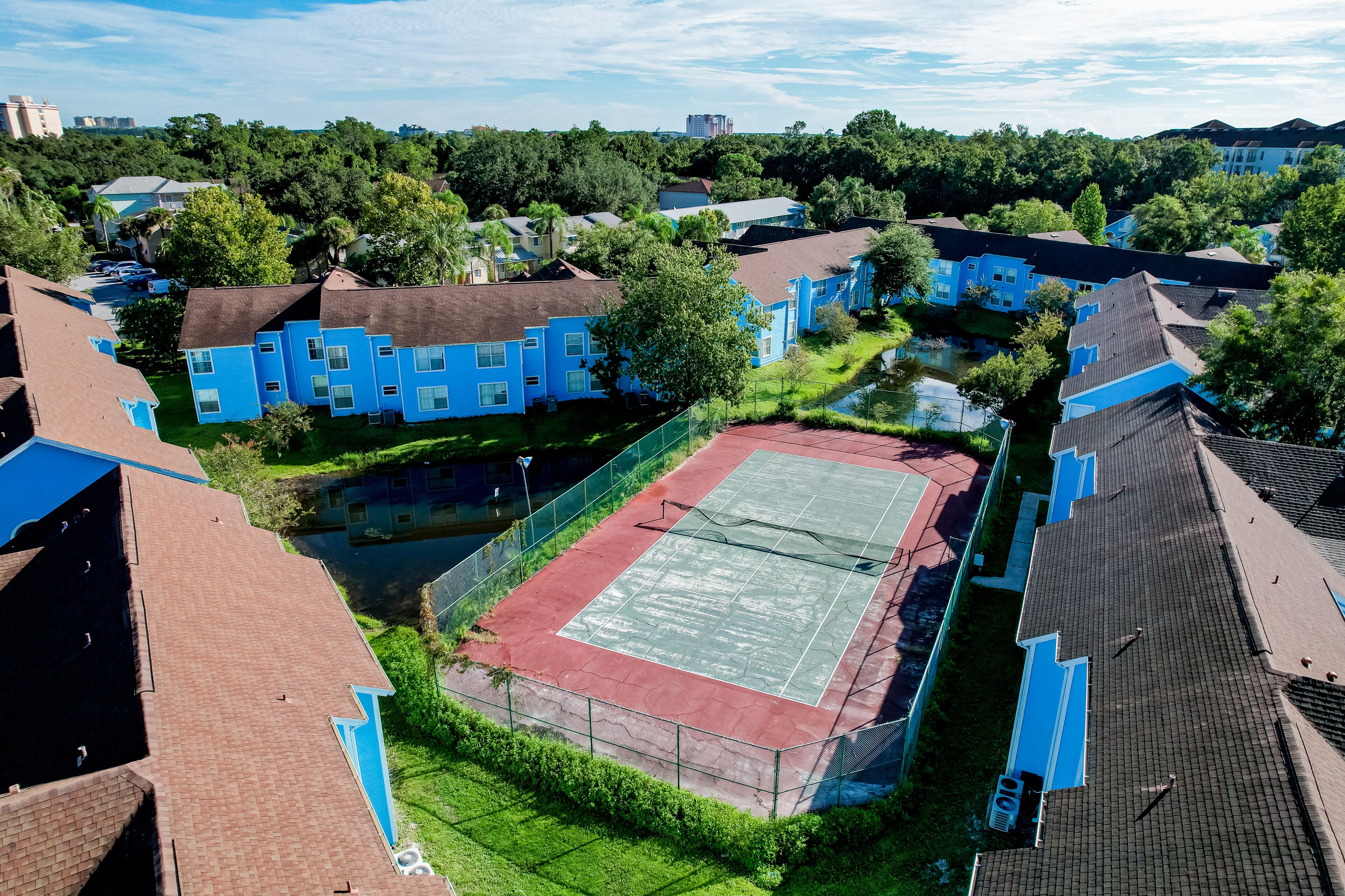 A residential area with blue houses, a tennis court, and surrounding greenery.