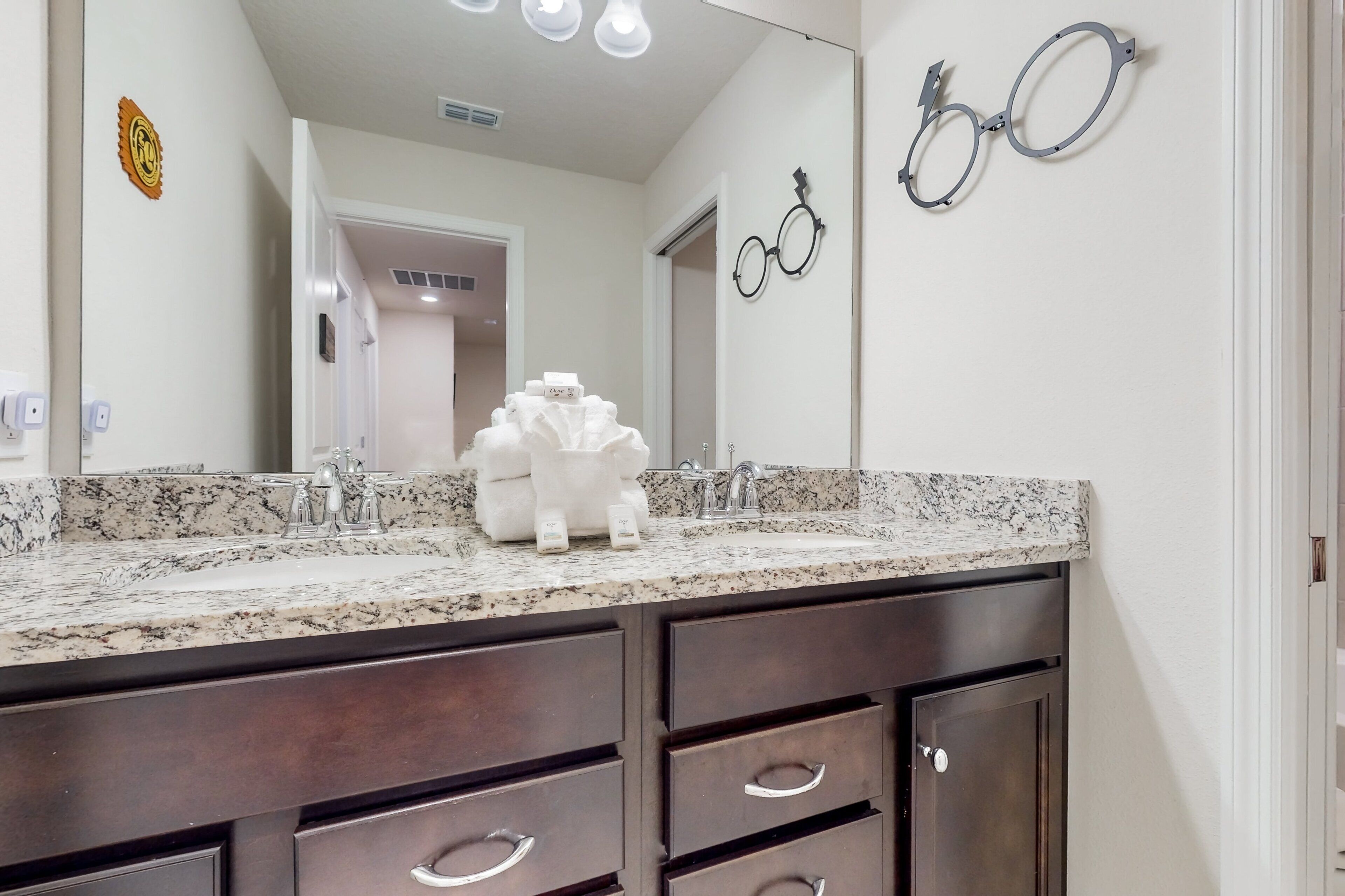 A bathroom with a granite countertop, dark wooden cabinets, a large mirror, and a towel rack.