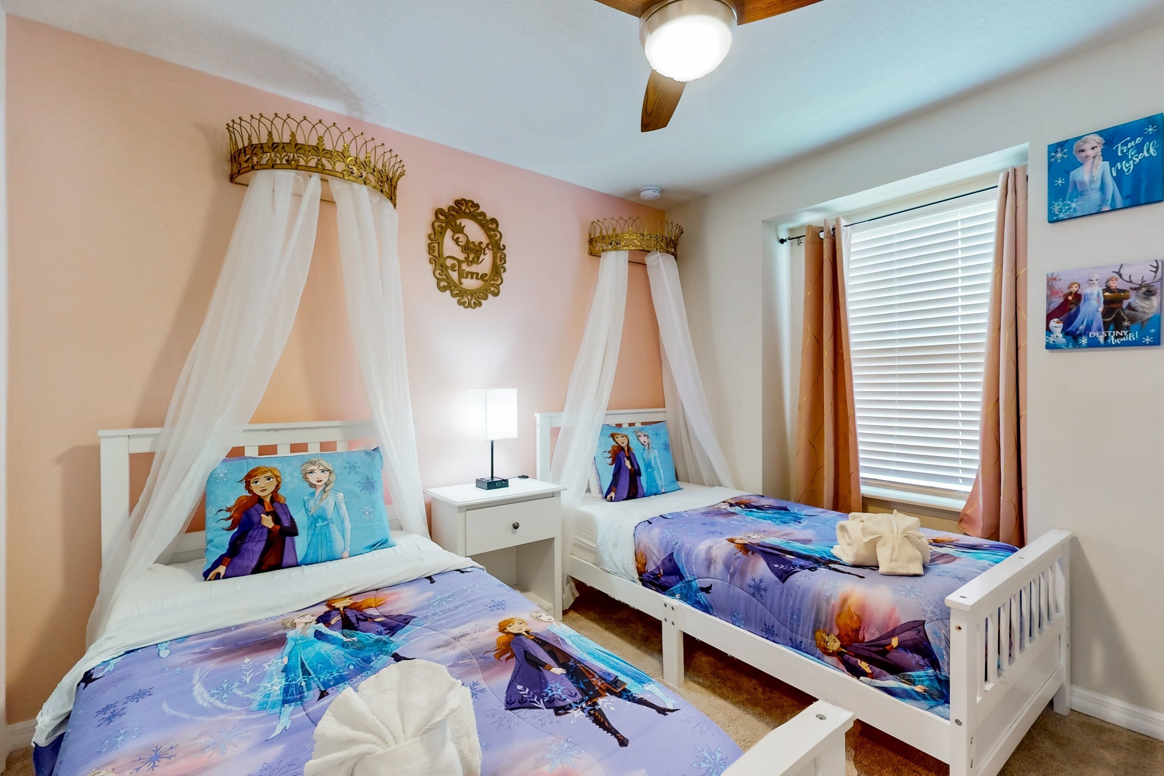Une chambre avec deux lits, un ventilateur de plafond, une table de chevet et une fenêtre avec des rideaux.