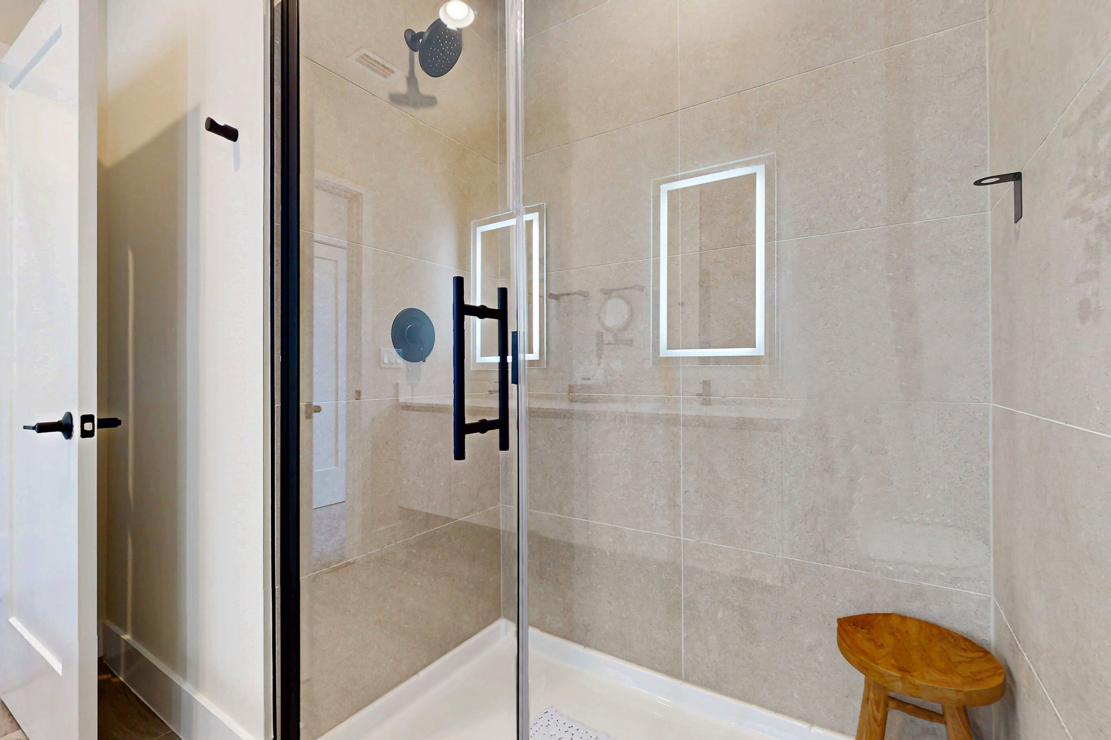 A glass-enclosed shower area with a wooden stool, tiled walls, and a visible door.