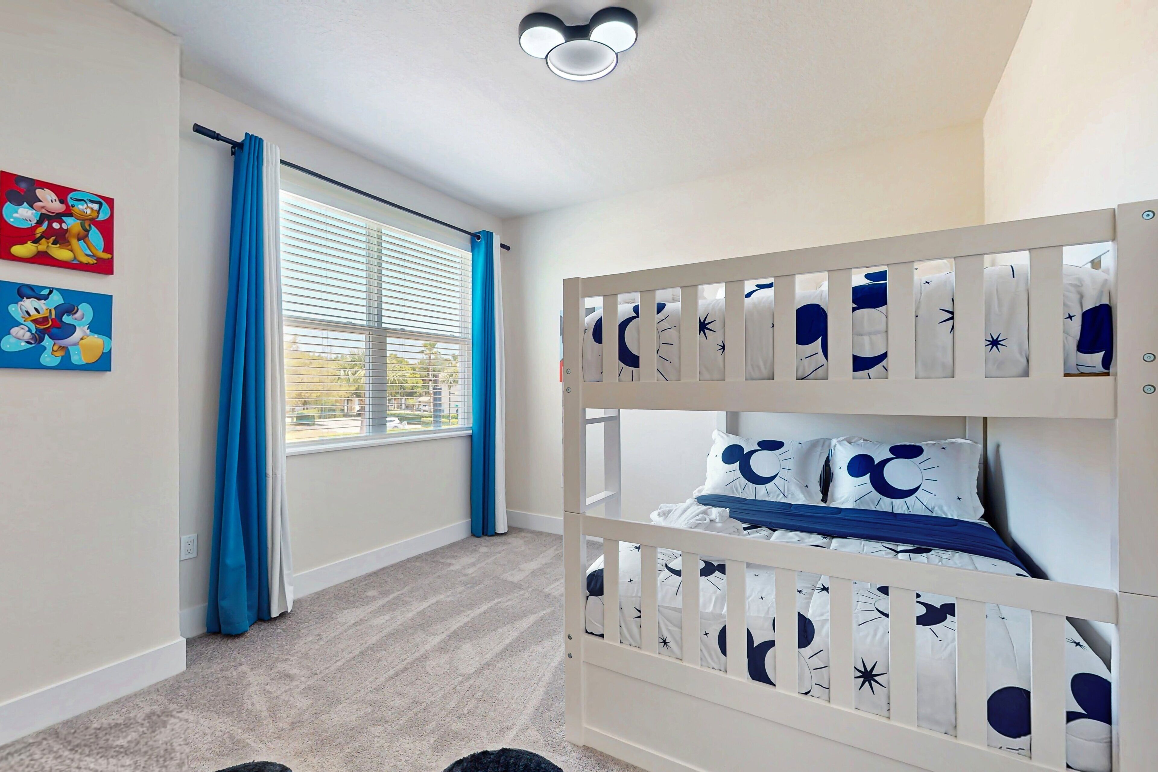 A child's bedroom with bunk beds, a window with curtains, and wall art.