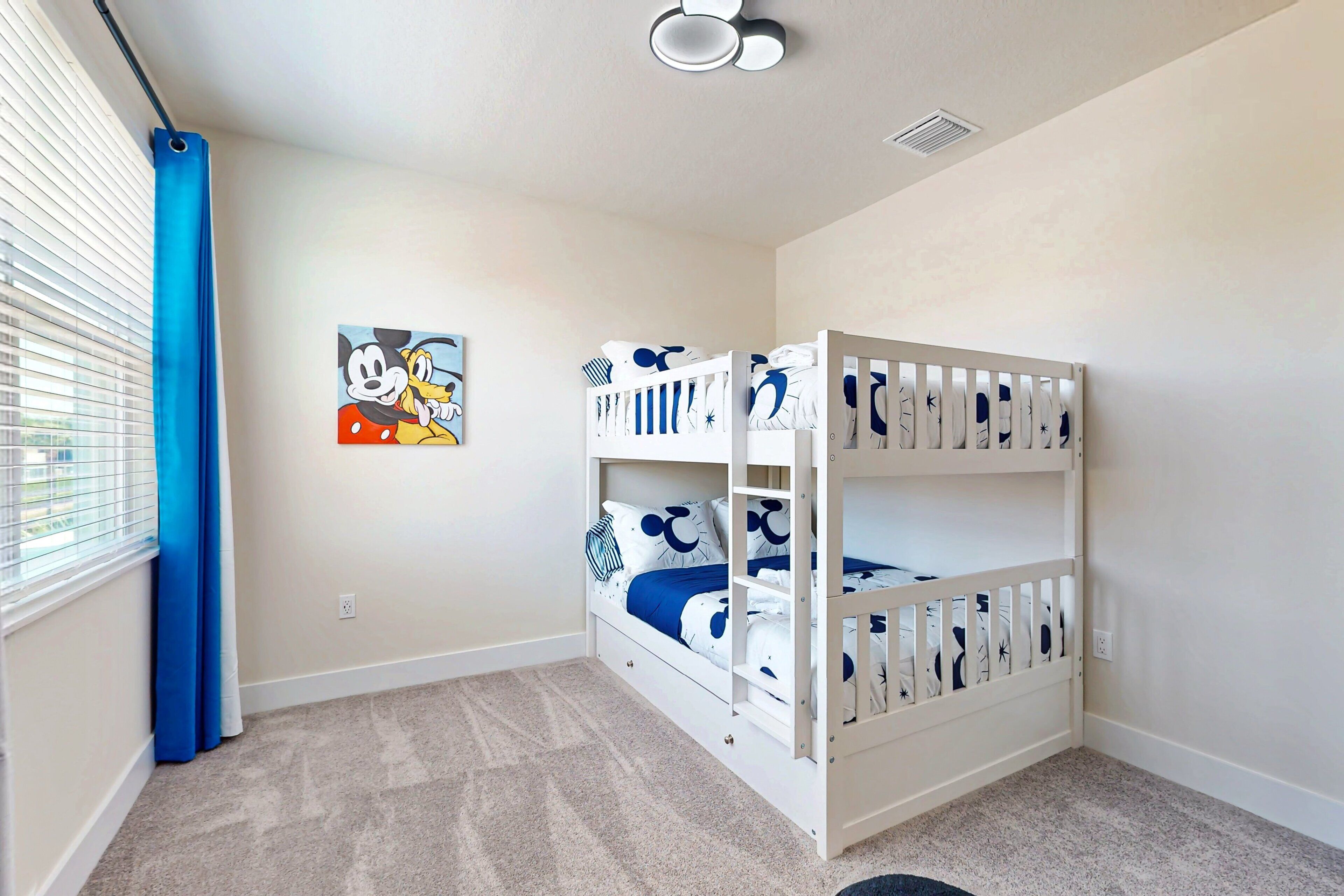 A room with a bunk bed, a window with blue curtains, a wall-mounted picture, and a carpeted floor.