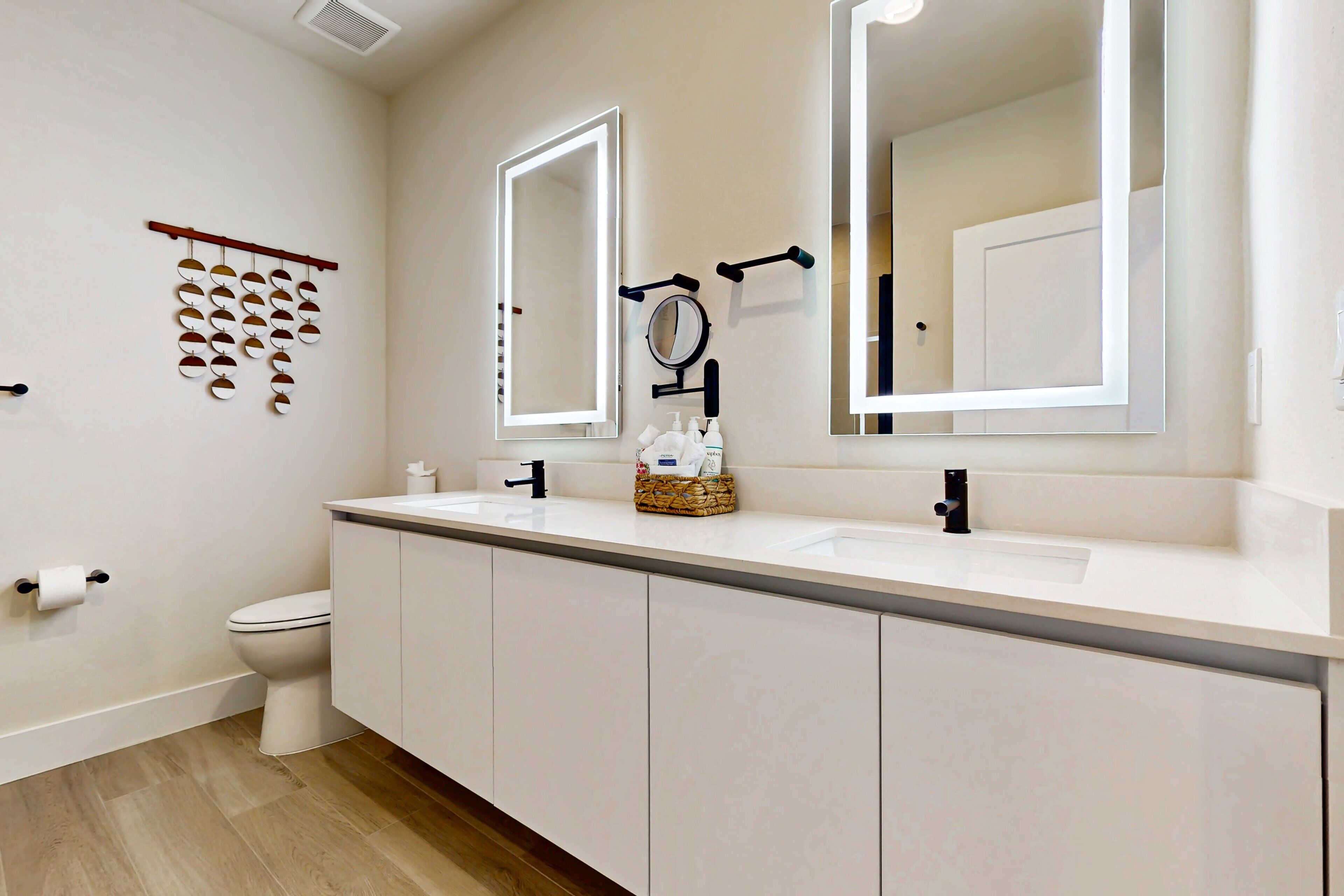 A modern bathroom with a white sink, two mirrors, a toilet, and a wooden floor.