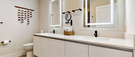 A modern bathroom with a white sink, two mirrors, a toilet, and a wooden floor.