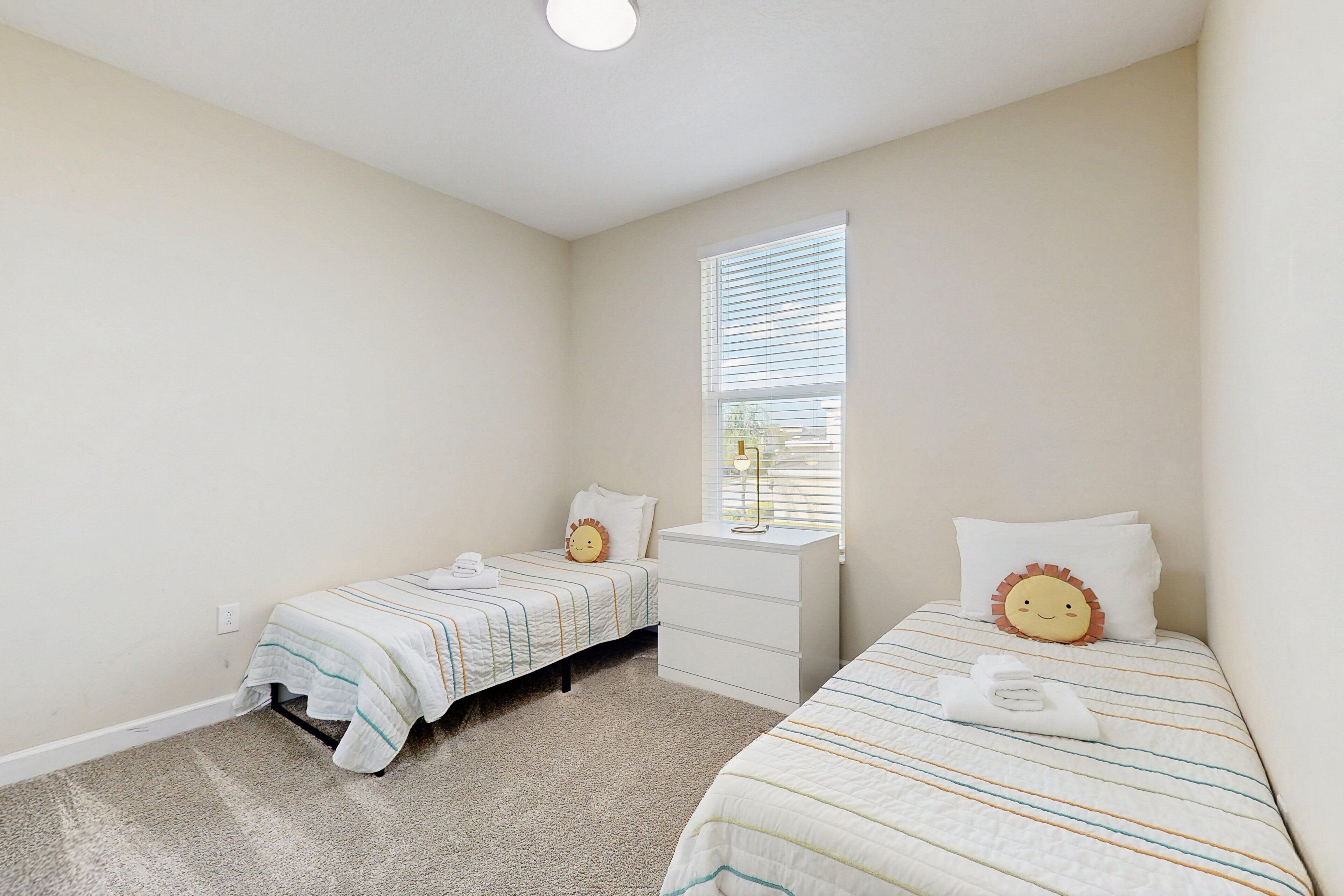 A bedroom with two beds, a window with blinds, a white dresser, and a carpeted floor.