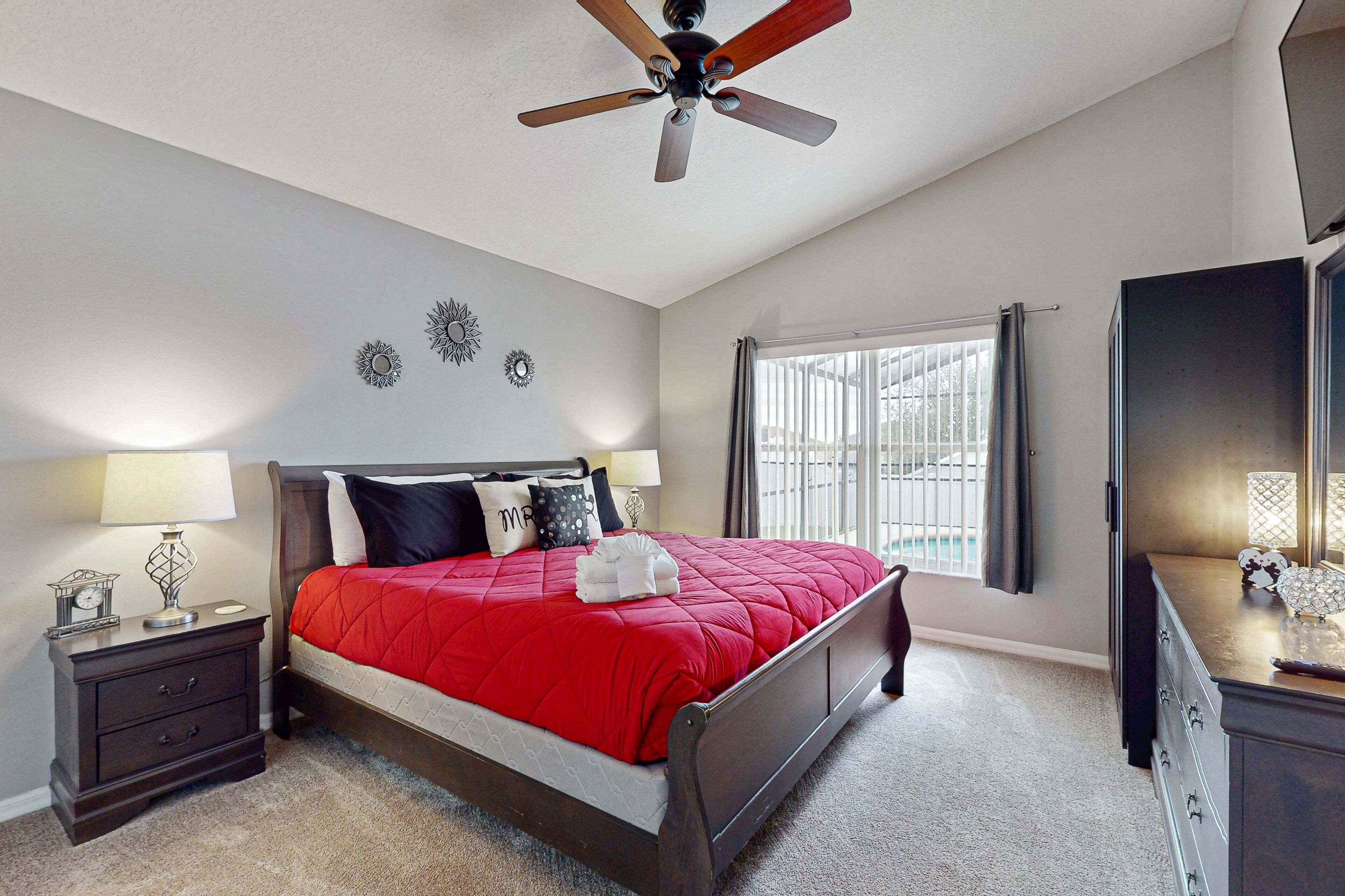 A bedroom with a bed, nightstand, dresser, ceiling fan, and window with curtains.