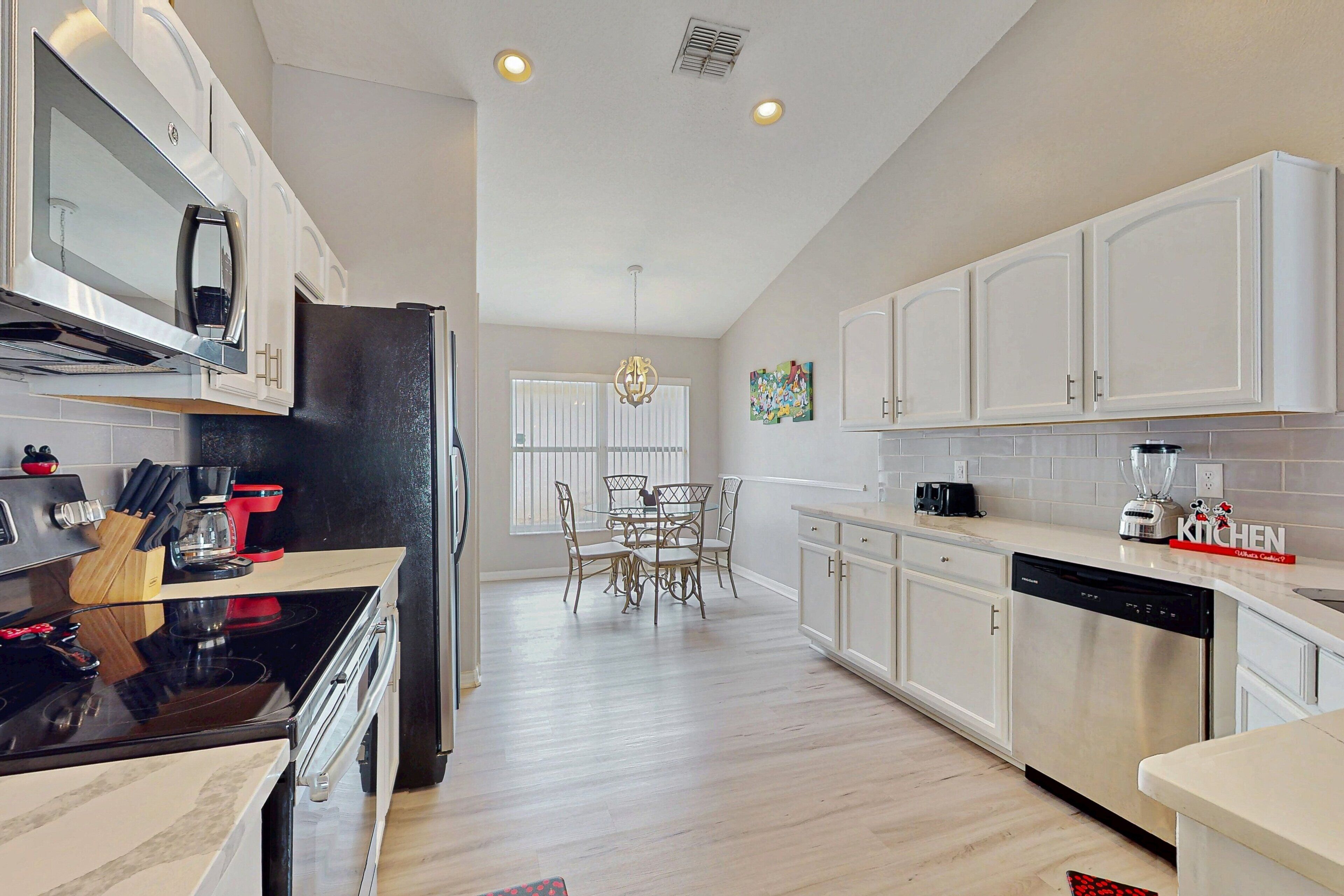 A modern kitchen with white cabinets, stainless steel appliances, and a dining area with a chandelier.