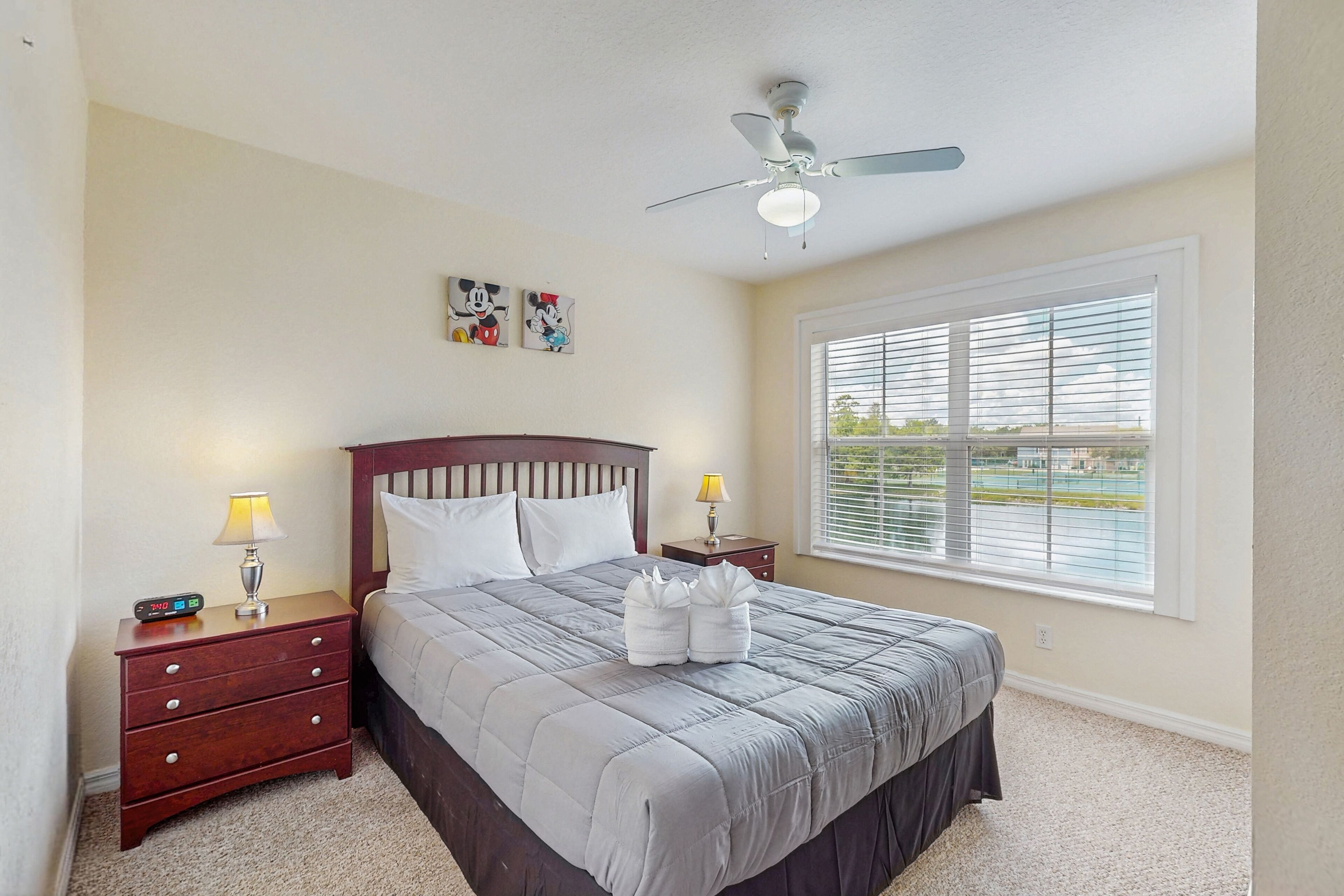 A bedroom with a bed, nightstands, a ceiling fan, and a window with blinds.