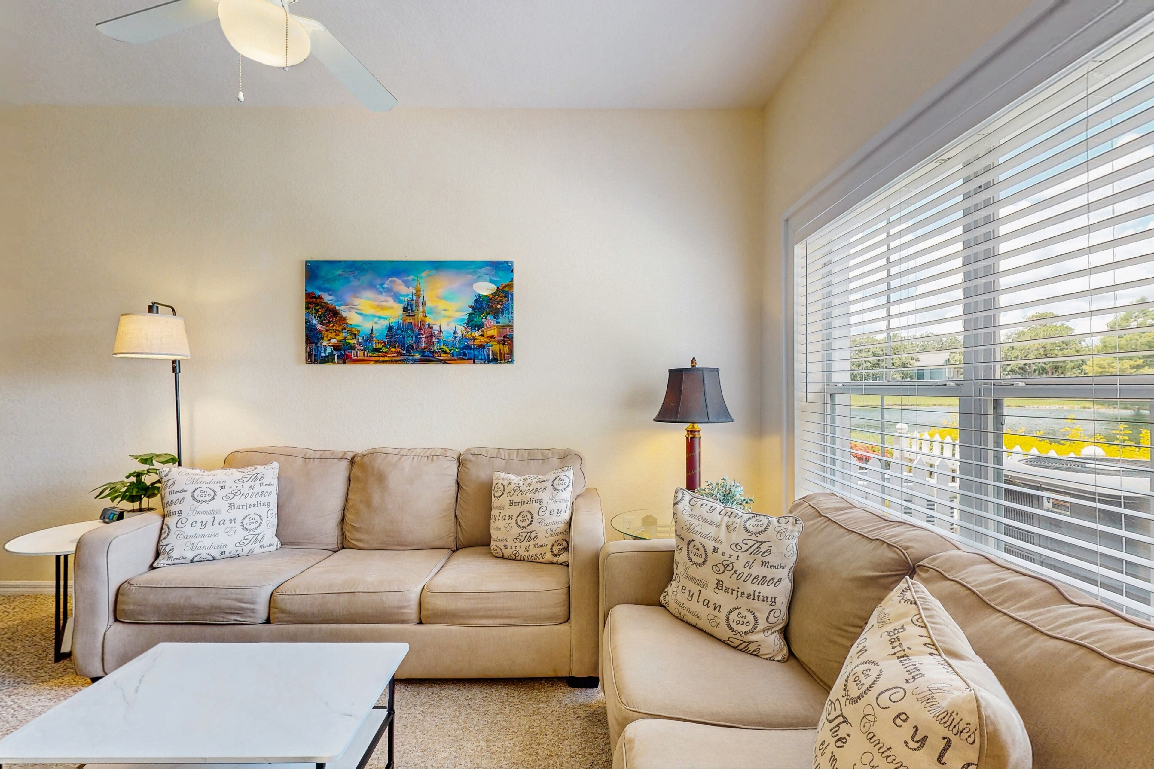 A living room with a beige sofa, two lamps, a painting, and a window with blinds.