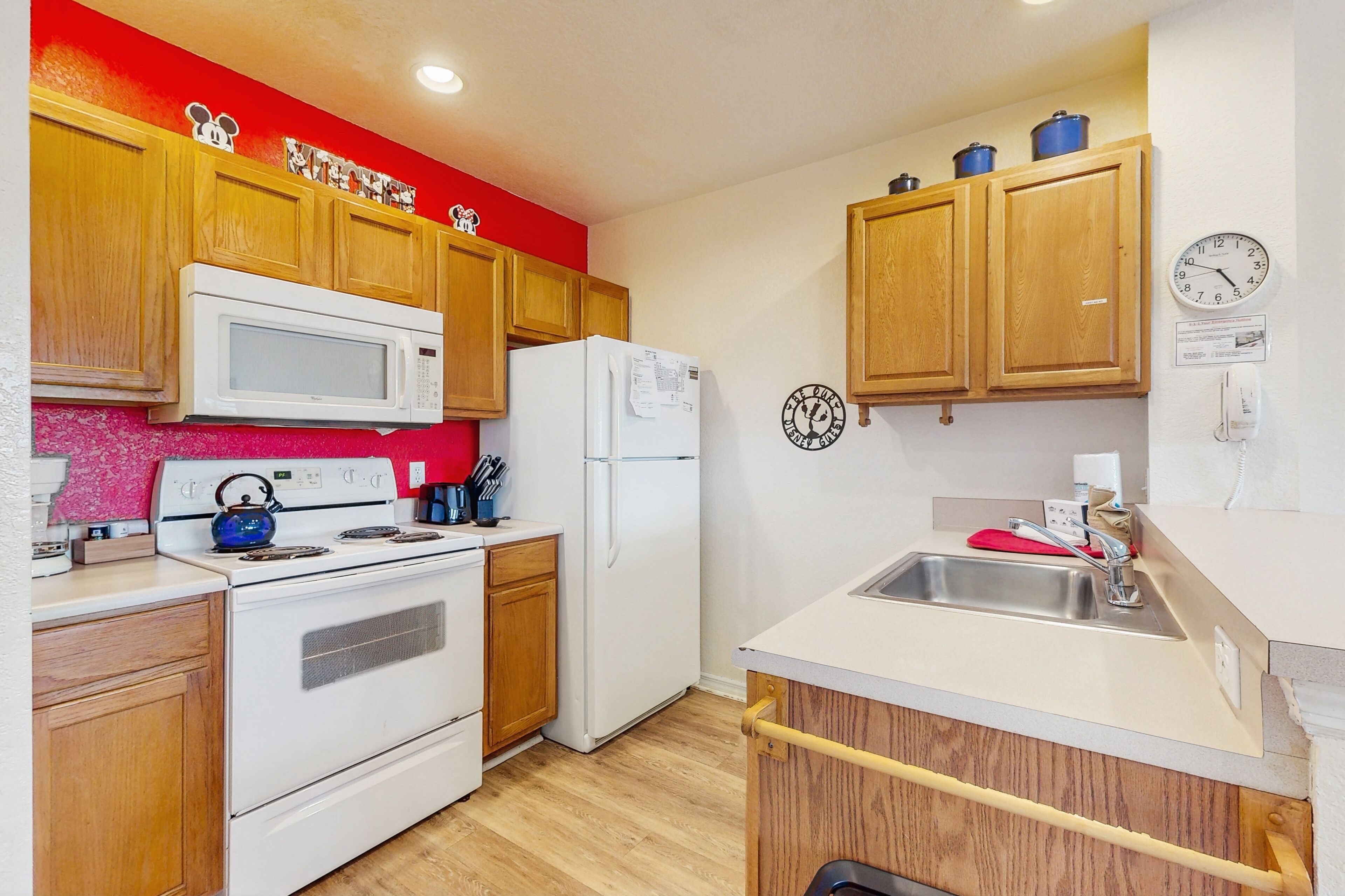 A compact kitchen with wooden cabinets, a microwave, a refrigerator, a stove, and a sink.