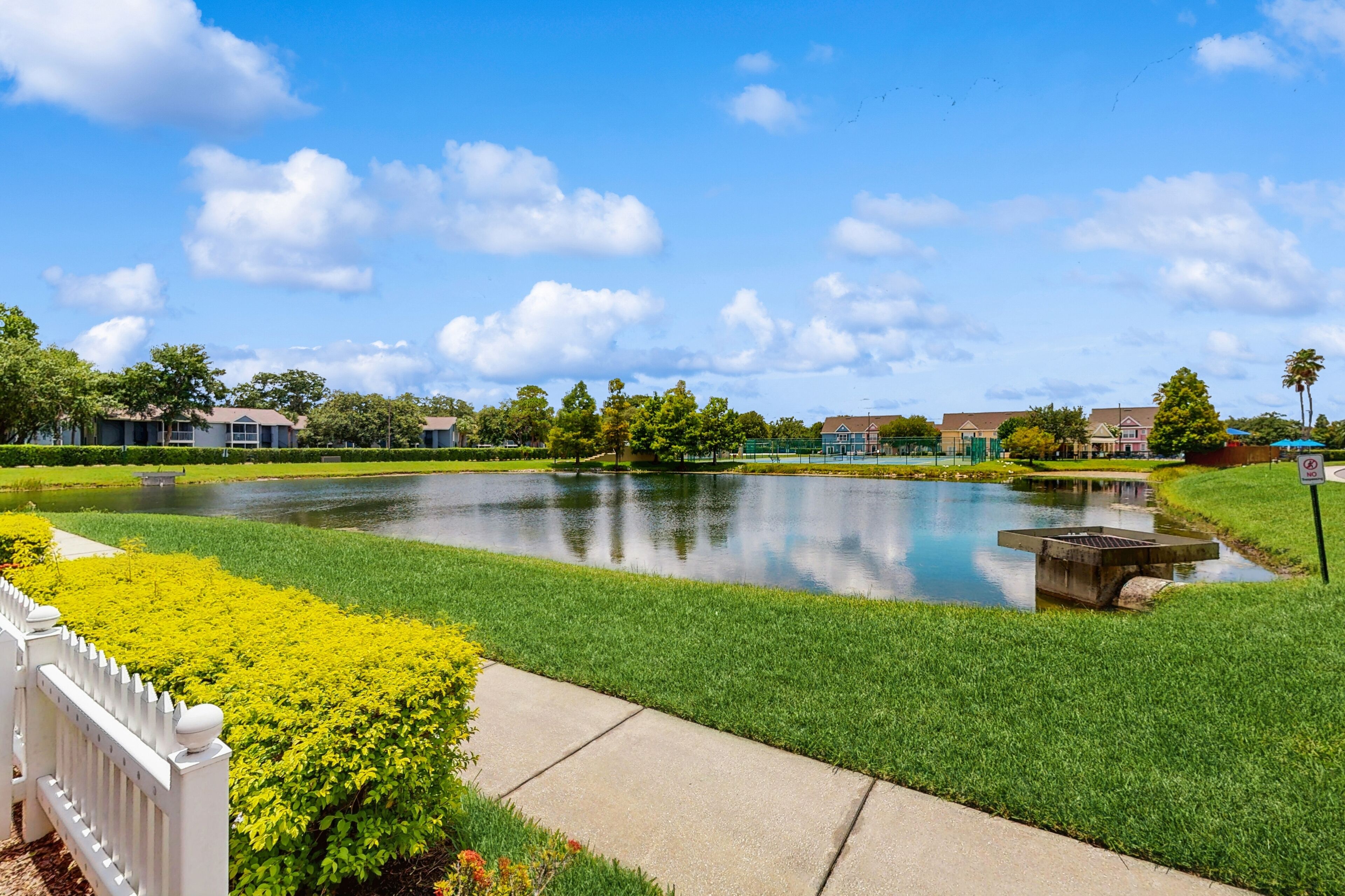 A serene outdoor area with a pond, well-maintained grass, and a white fence.