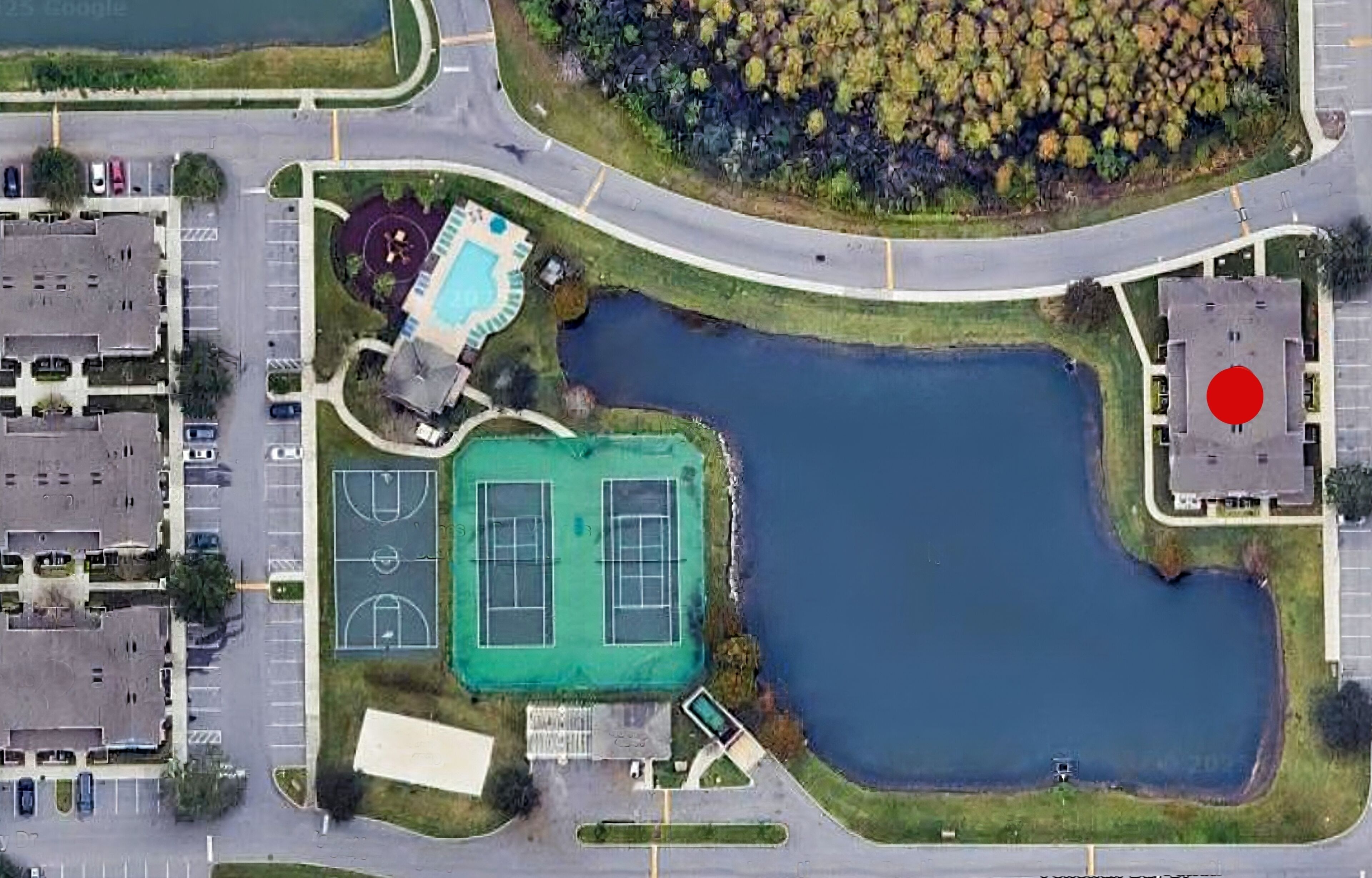 An aerial view of a residential area with a large pond, tennis courts, and a swimming pool.