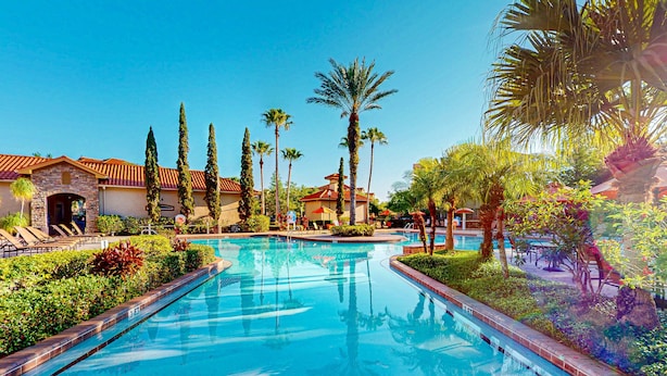 A swimming pool with a tiled deck, surrounded by palm trees and a building with a red-tiled roof. - Resort Condo With Heated Pool, Gym, BBQ Area, Balcony, W/d, Children's Pool, AC (Davenport)