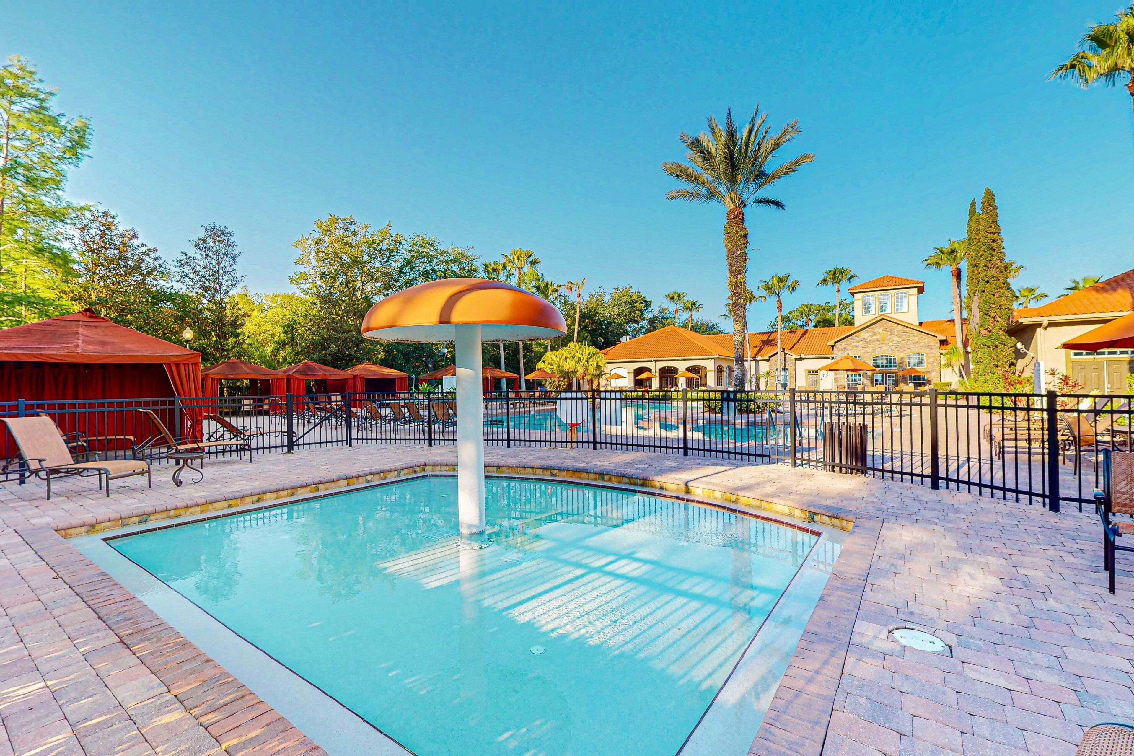 A swimming pool with lounge chairs, a palm tree, and a building with a tiled roof.