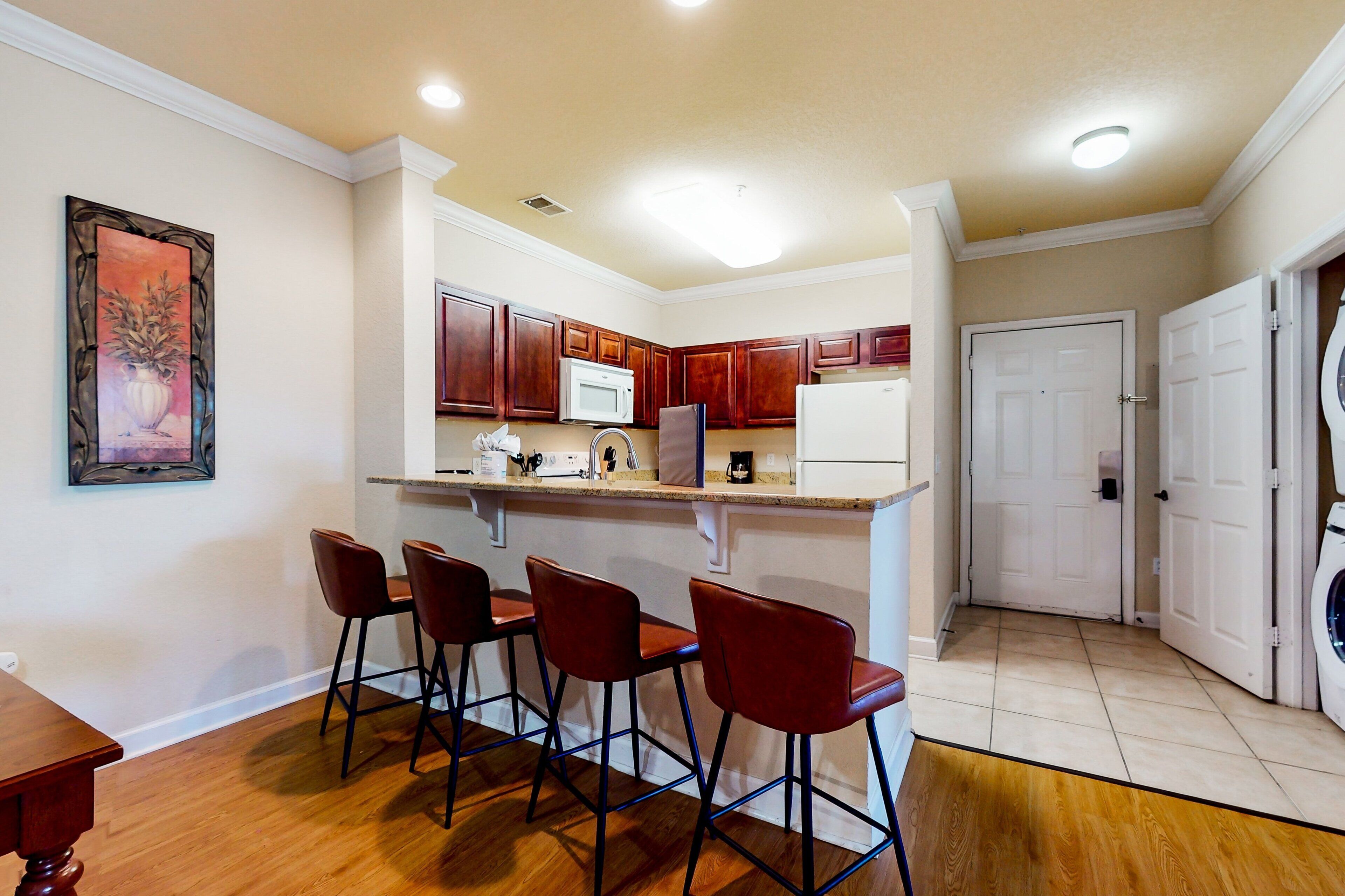 A kitchen with a bar area, a microwave, a refrigerator, and a washing machine.