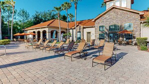 A hotel with a patio area featuring sun loungers and a stone building with arched windows. - Resort Condo With Heated Pool, Gym, BBQ Area, Balcony, W/d, Children's Pool, AC (Davenport)