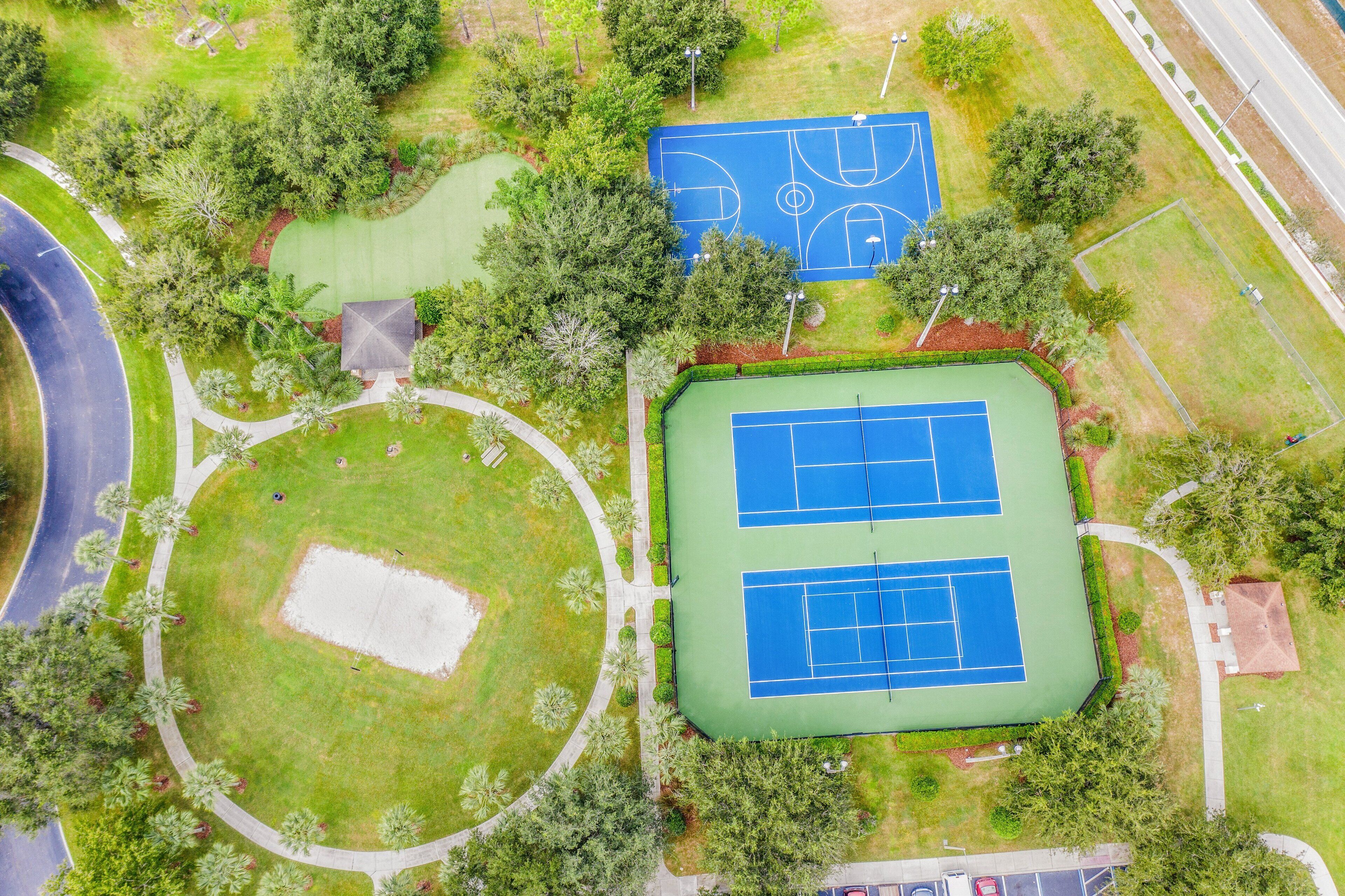 An aerial view of a park with a tennis court, a circular green space, and a building with a sloped roof.