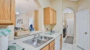 A kitchen with two sinks, wooden cabinets, and a countertop with a basket and a phone. - Friendly Condo With Pool and hot tub Access, Wifi, Central AC, and Private W/D (Kissimmee)