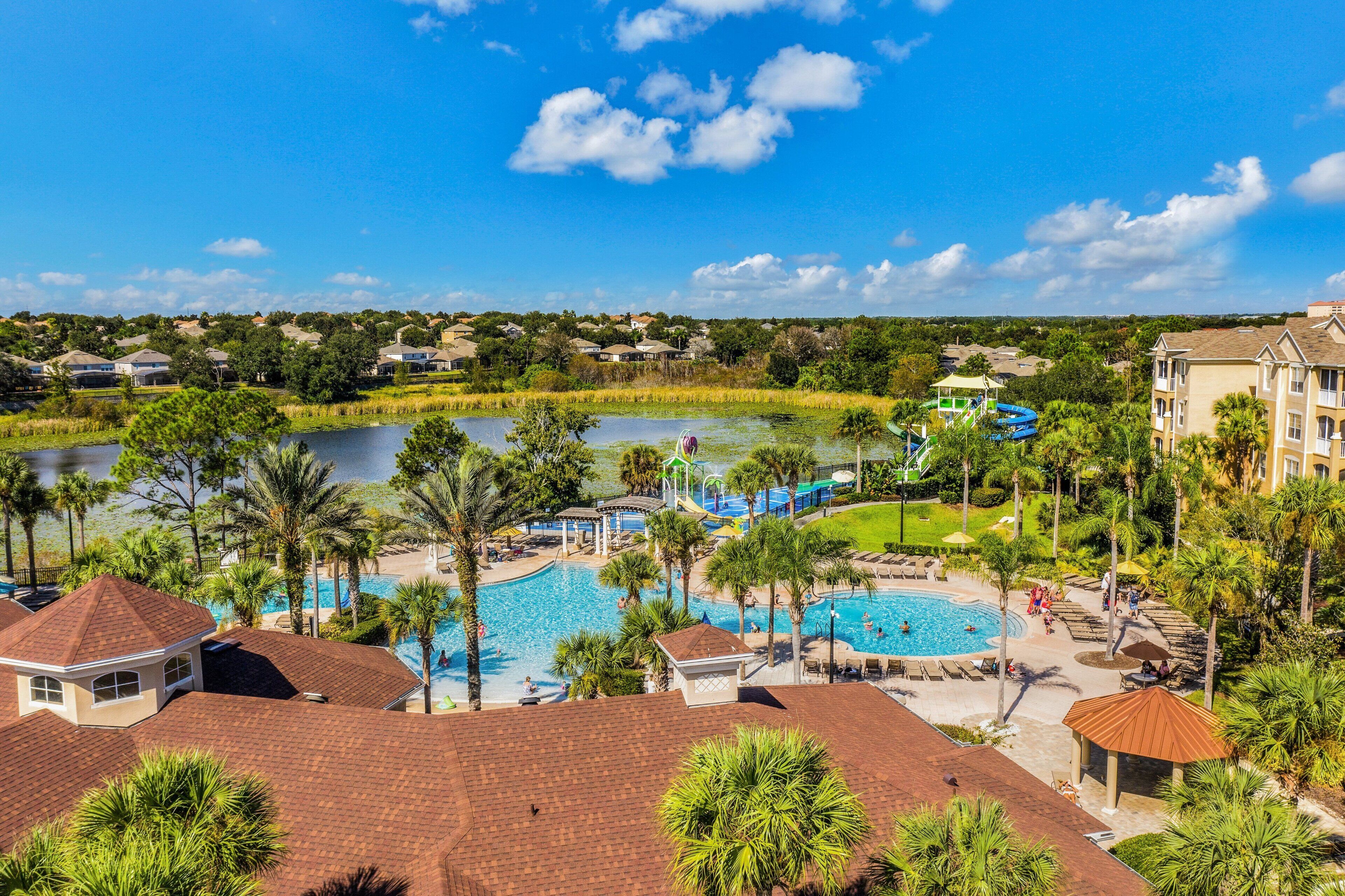 A resort with a large swimming pool, palm trees, and a view of a lake.