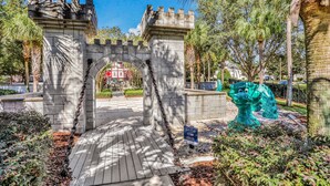 A stone archway entrance with a chain gate, a wooden pathway, and a green sculpture. - Friendly Condo With Pool and hot tub Access, Wifi, Central AC, and Private W/D (Kissimmee)