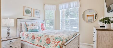 Un dormitorio con cama, mesita de noche, lámpara, ventana con persianas y un espejo en la pared.