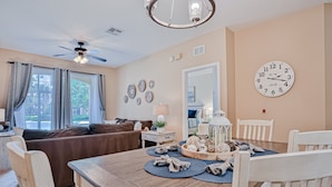 A dining area with a wooden table, chairs, a ceiling fan, and a wall clock. - Friendly Condo With Pool and hot tub Access, Wifi, Central AC, and Private W/D (Kissimmee)