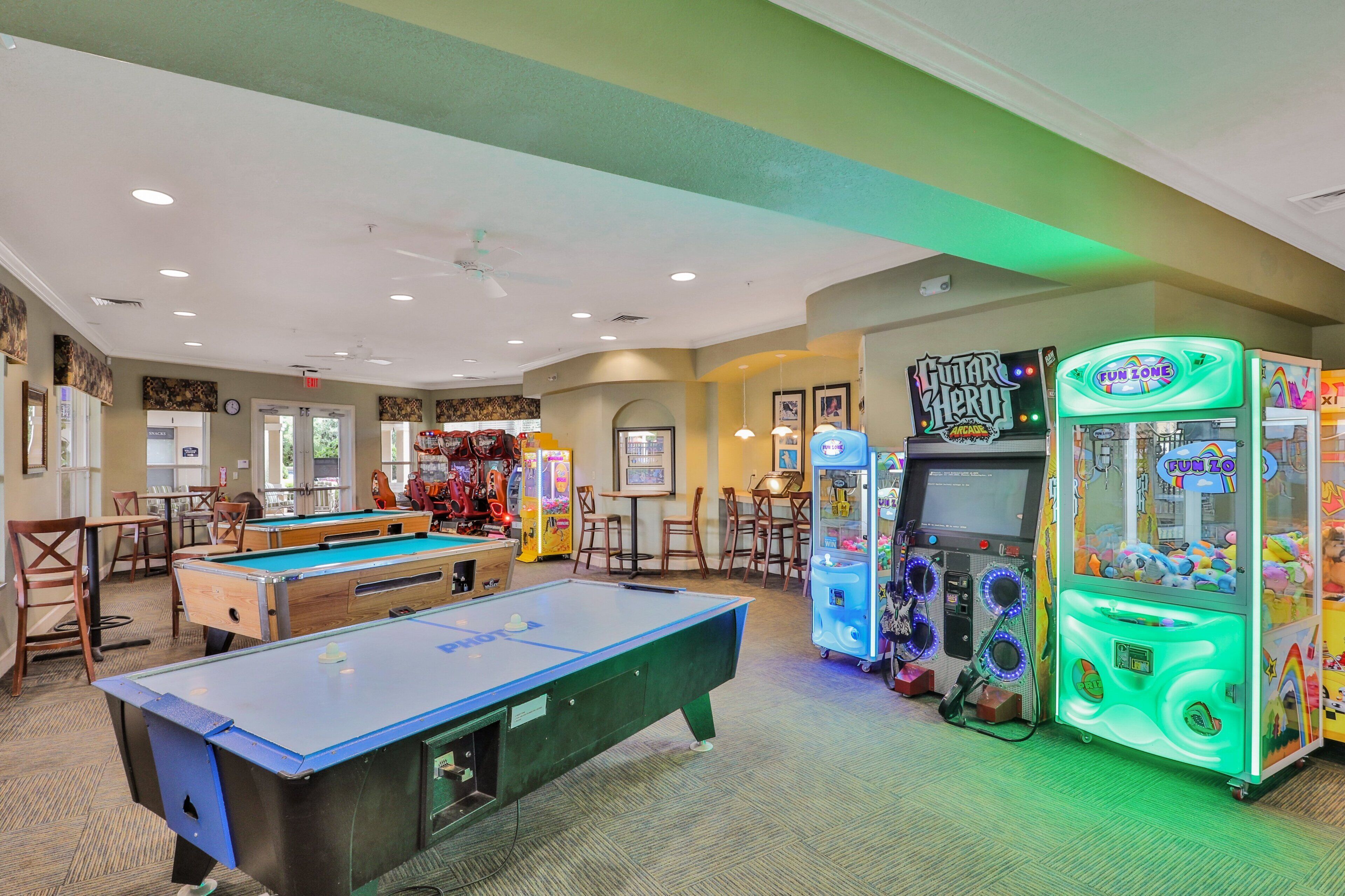 A pool table, arcade games, and a billiards table in a room with chairs and tables.