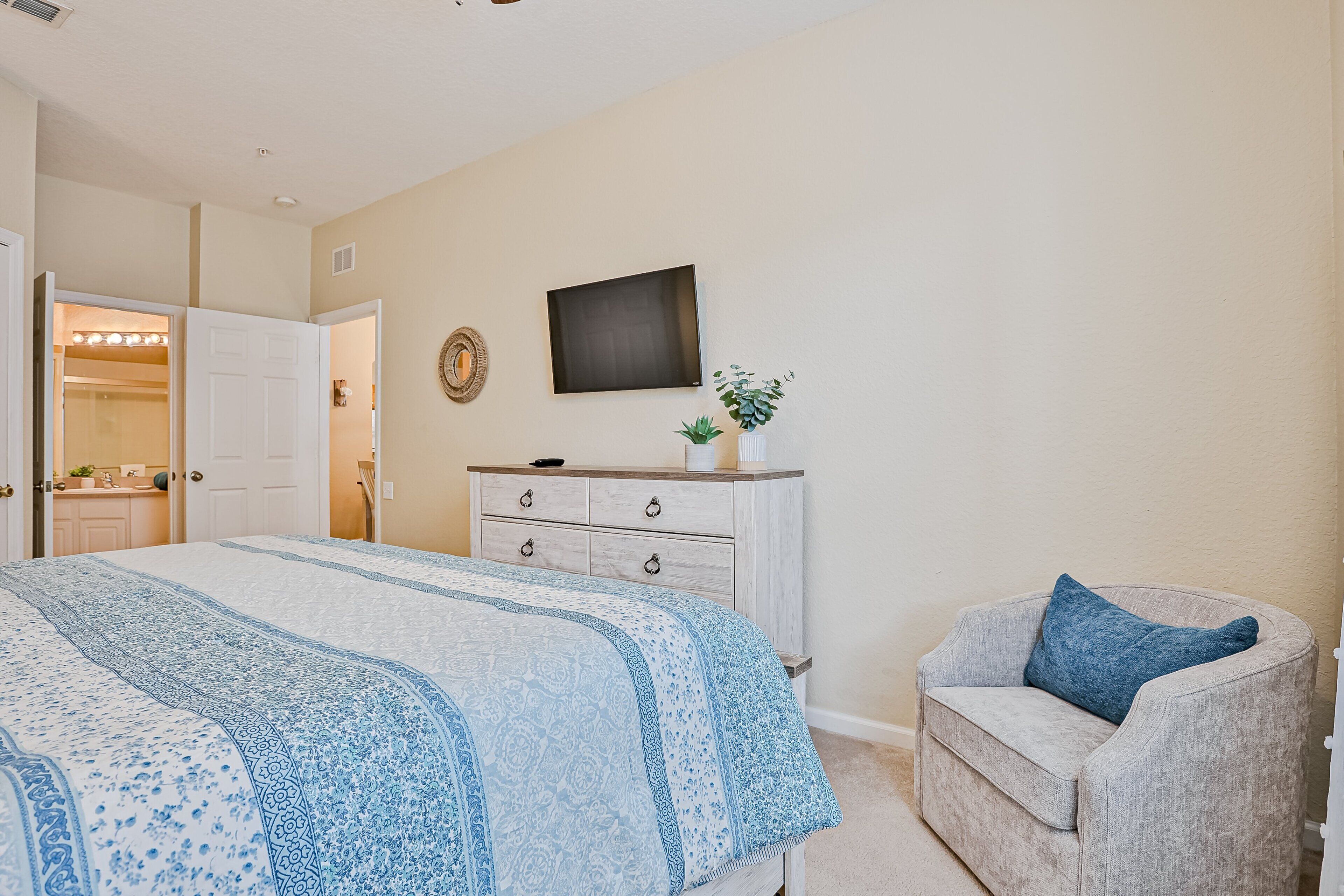 A bedroom with a bed, a dresser, a chair, and a television on the wall.