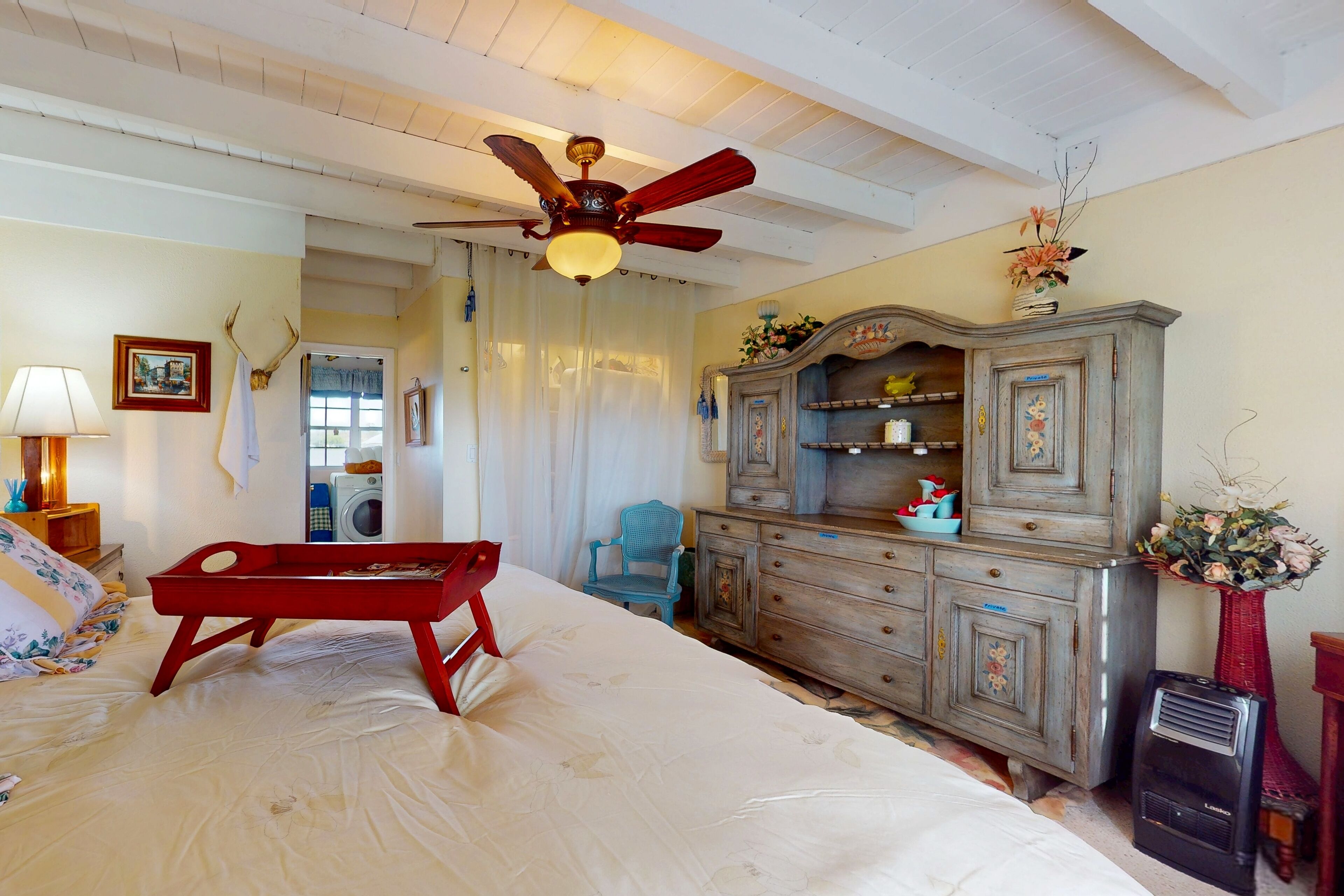 Een slaapkamer met een bed, een rode bank, een houten dressoir, een plafondventilator en een vintage radio.