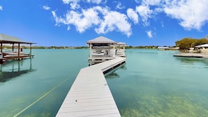 Un cielo azul despejado, un muelle de madera que lleva a una estructura cubierta y agua tranquila.