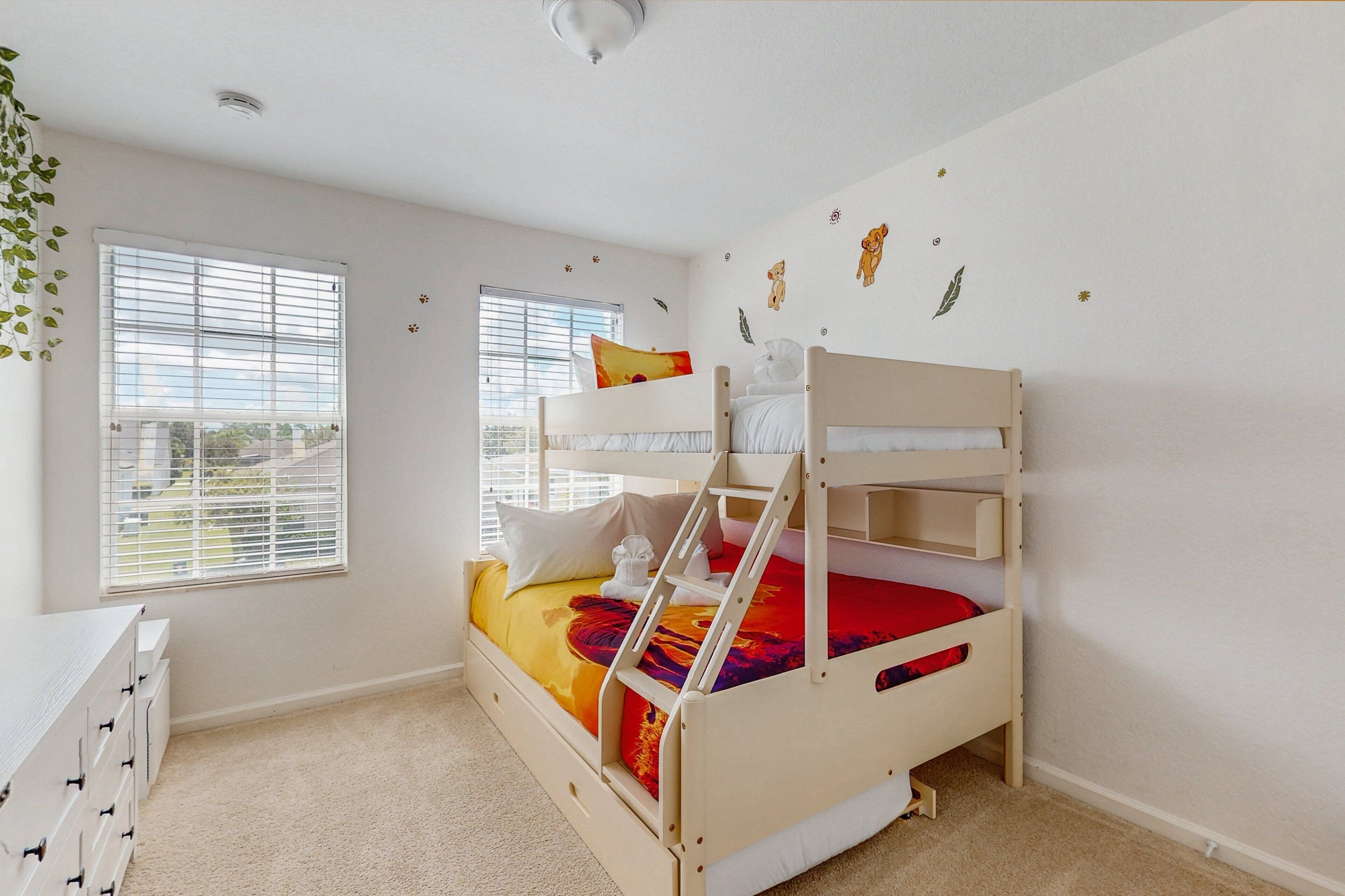 A bunk bed room with a desk, windows, and wall decorations.