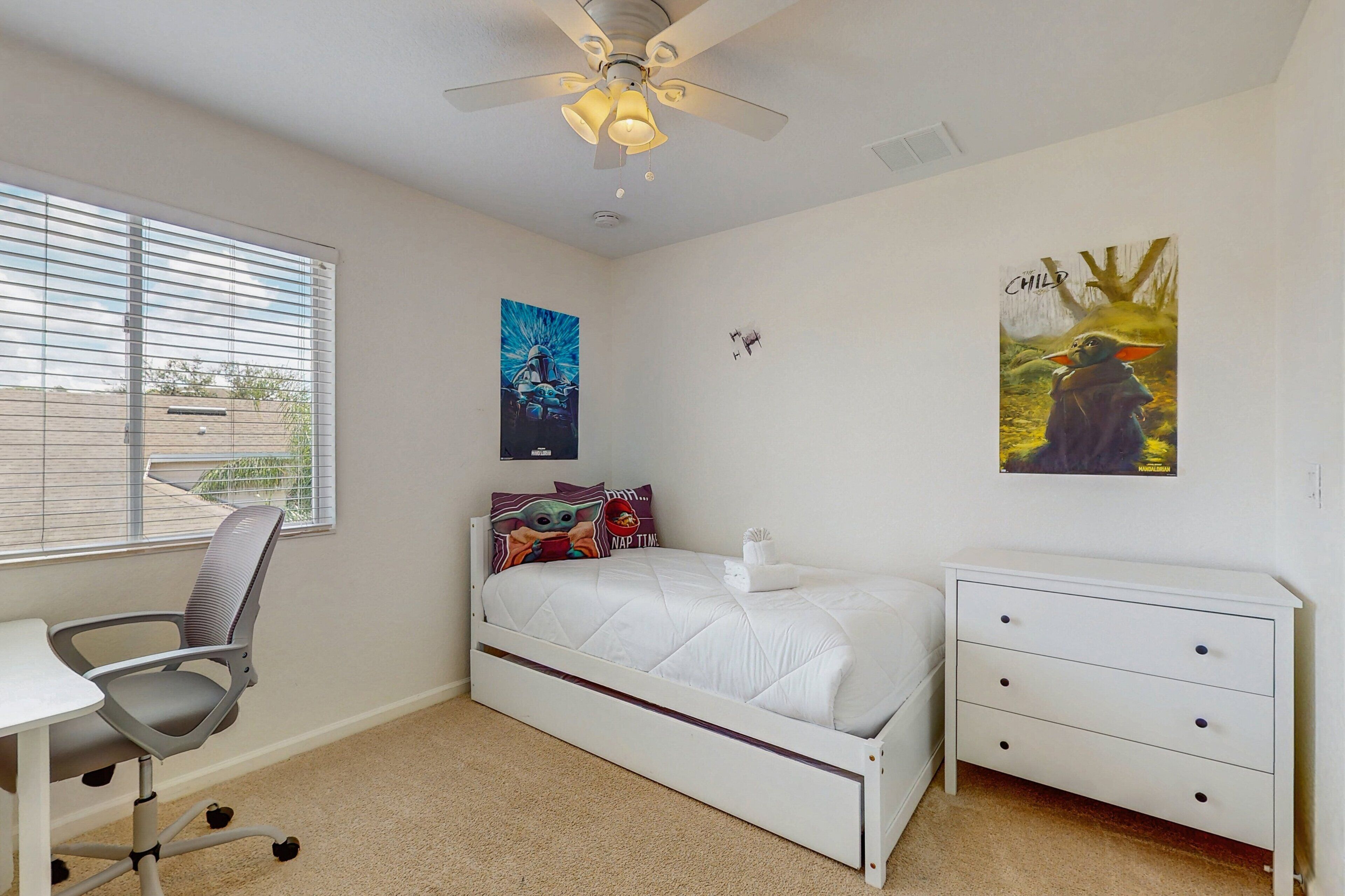 A bedroom with a bed, a desk, a chair, a dresser, and a ceiling fan.