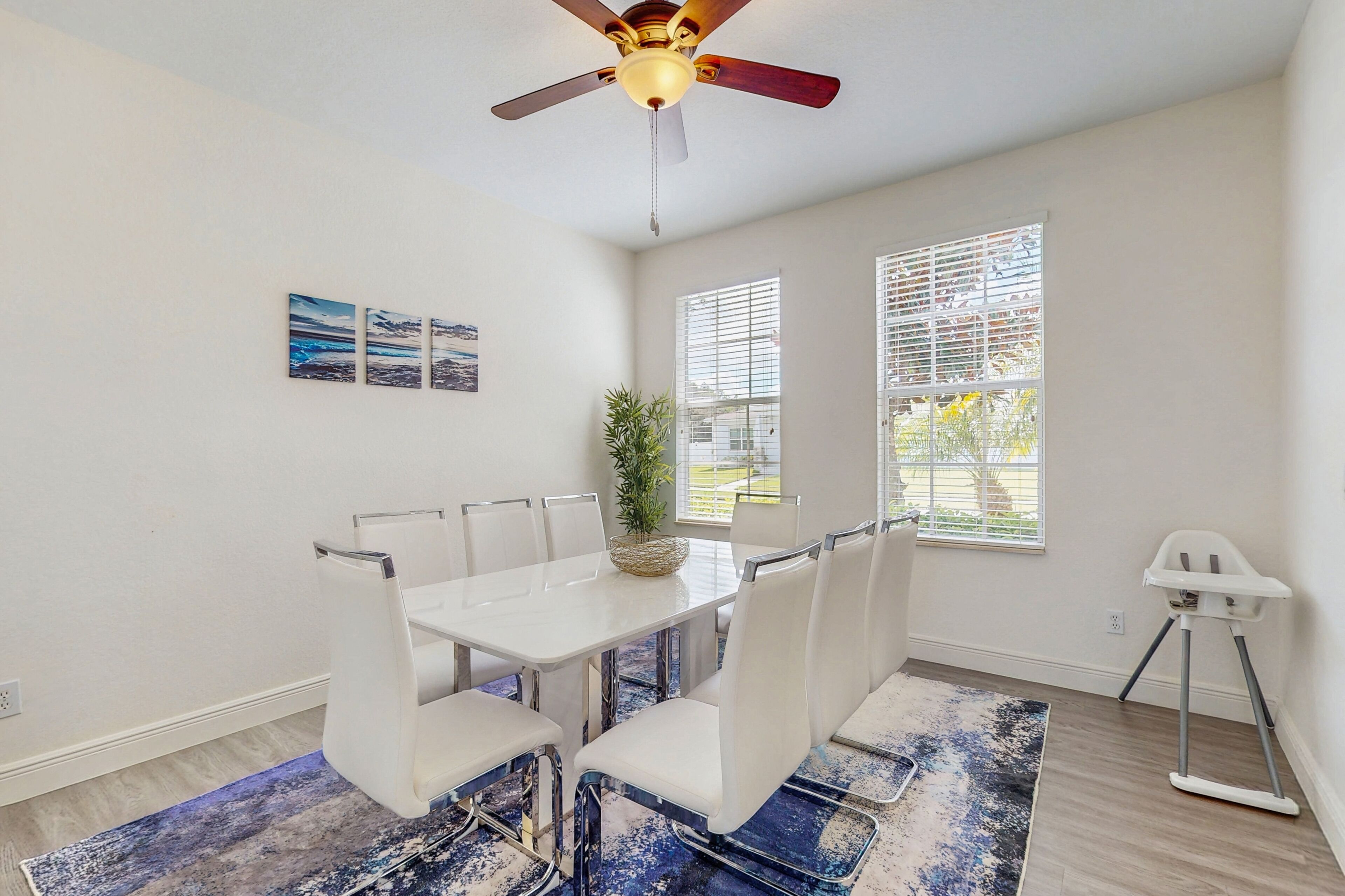 A dining area with a white table and chairs, a ceiling fan, and a window with blinds.