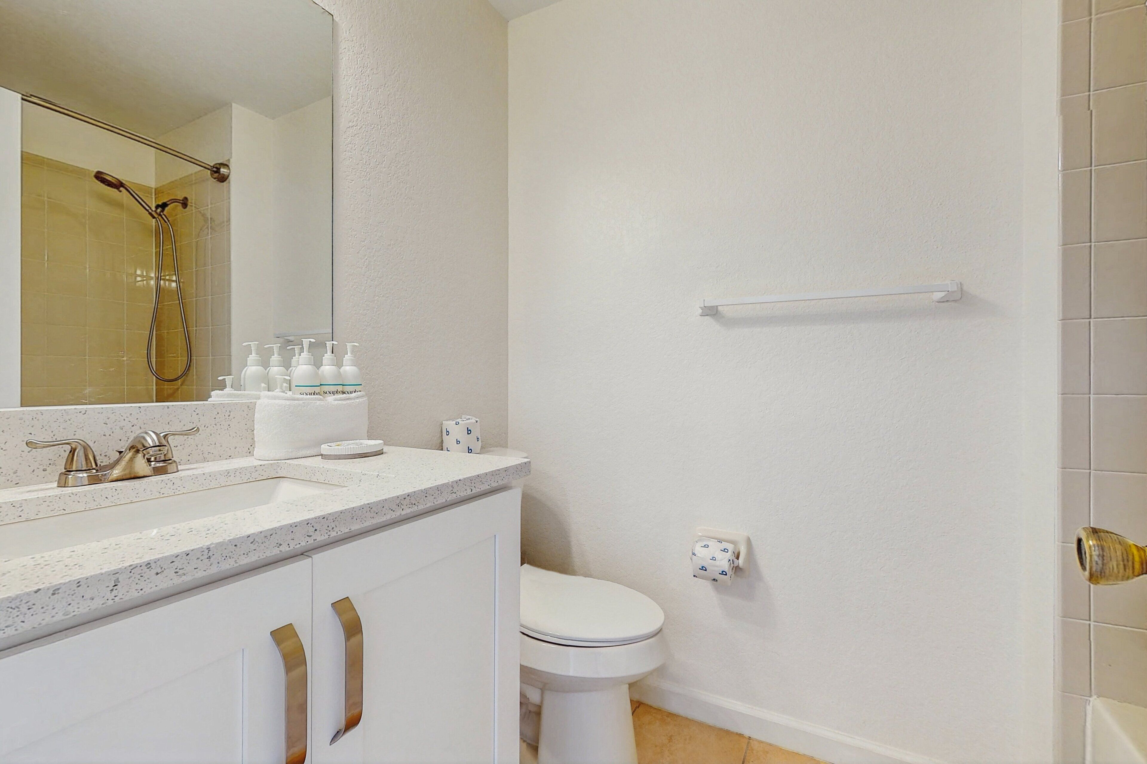 Un baño con lavamanos blanco, espejo, inodoro y zona de ducha.