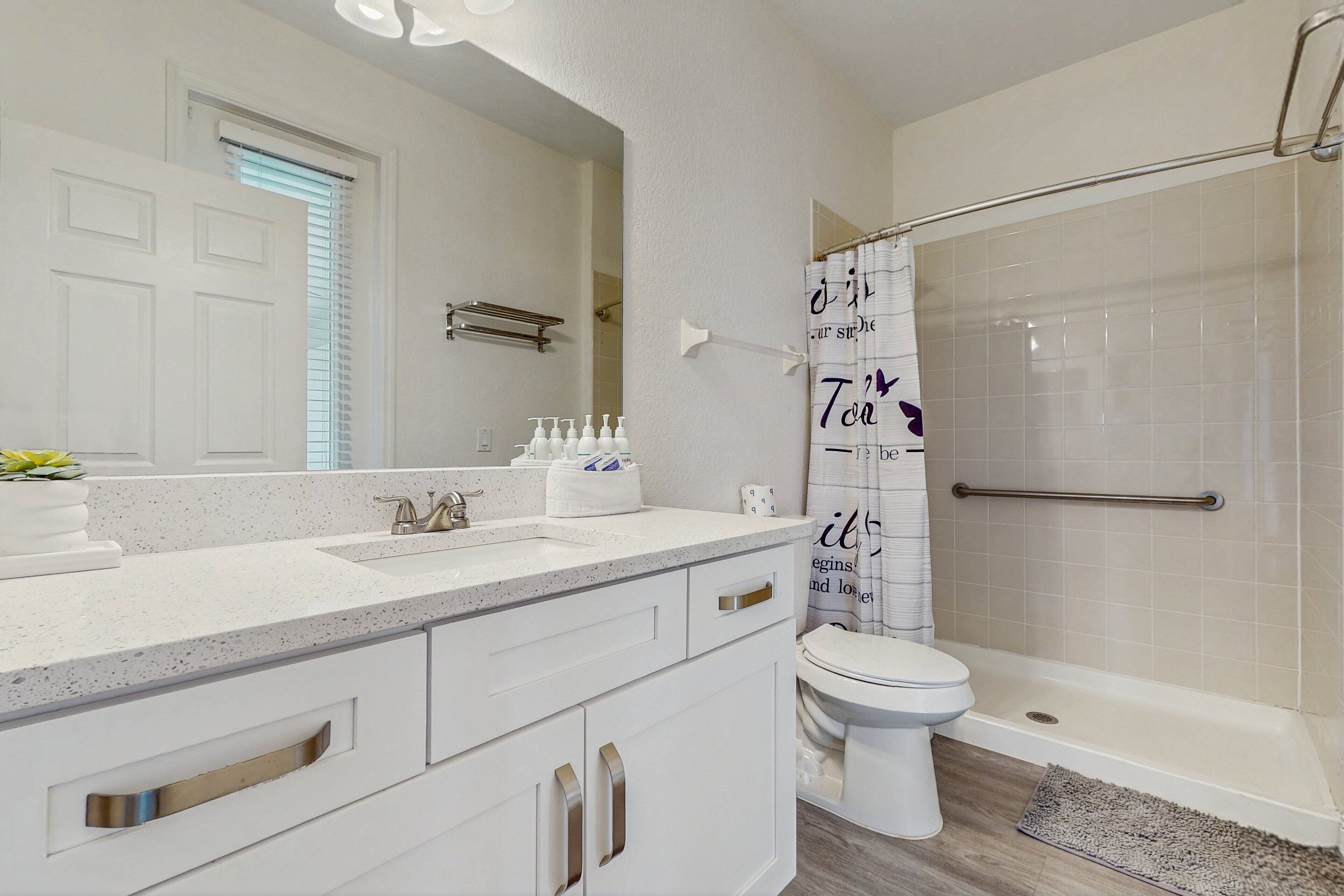 A bathroom with a white sink, mirror, toilet, and shower.