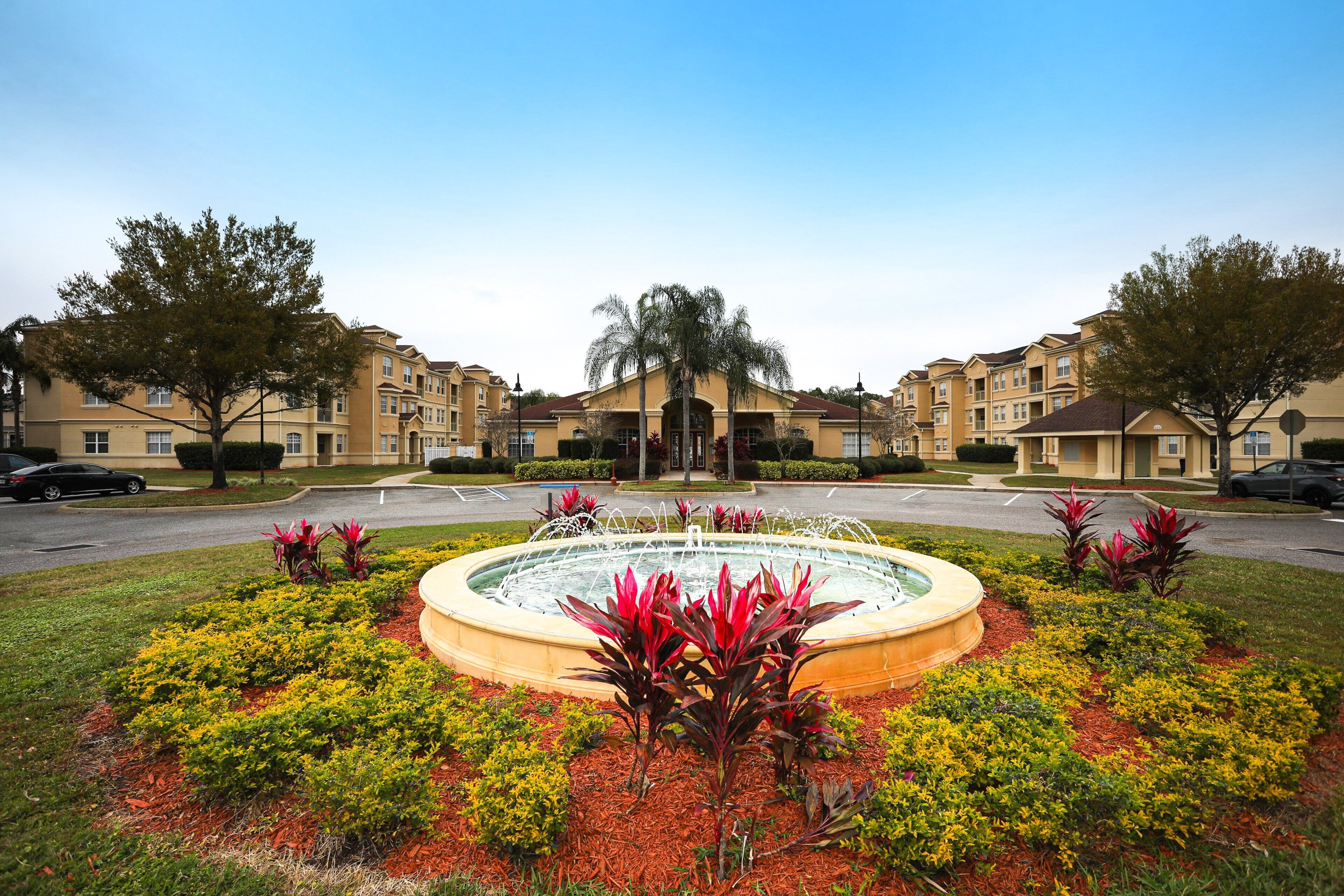 A residential area with a central fountain, surrounded by well-maintained landscaping and multi-story buildings.