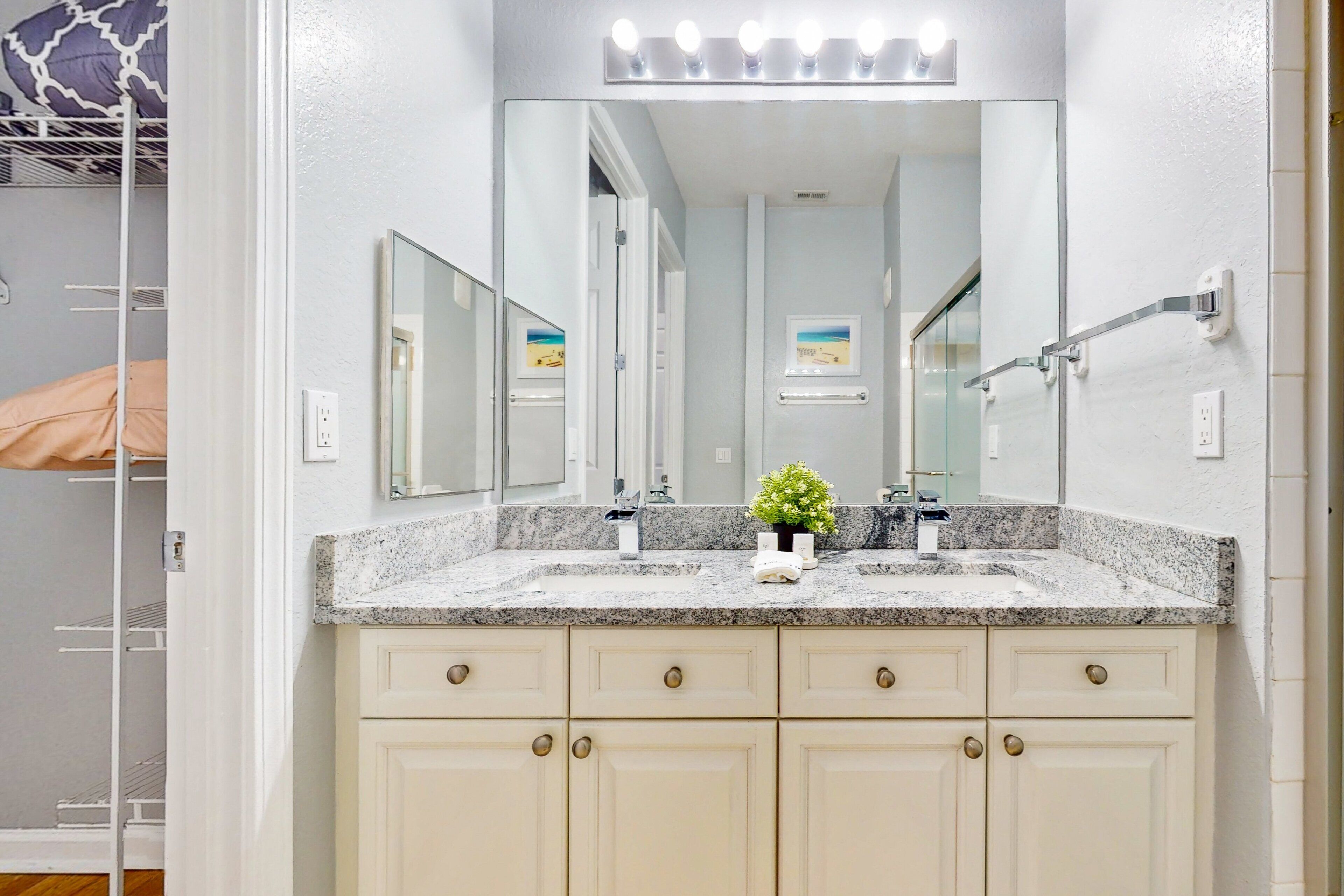 A bathroom with a granite countertop, a large mirror, and a small potted plant.