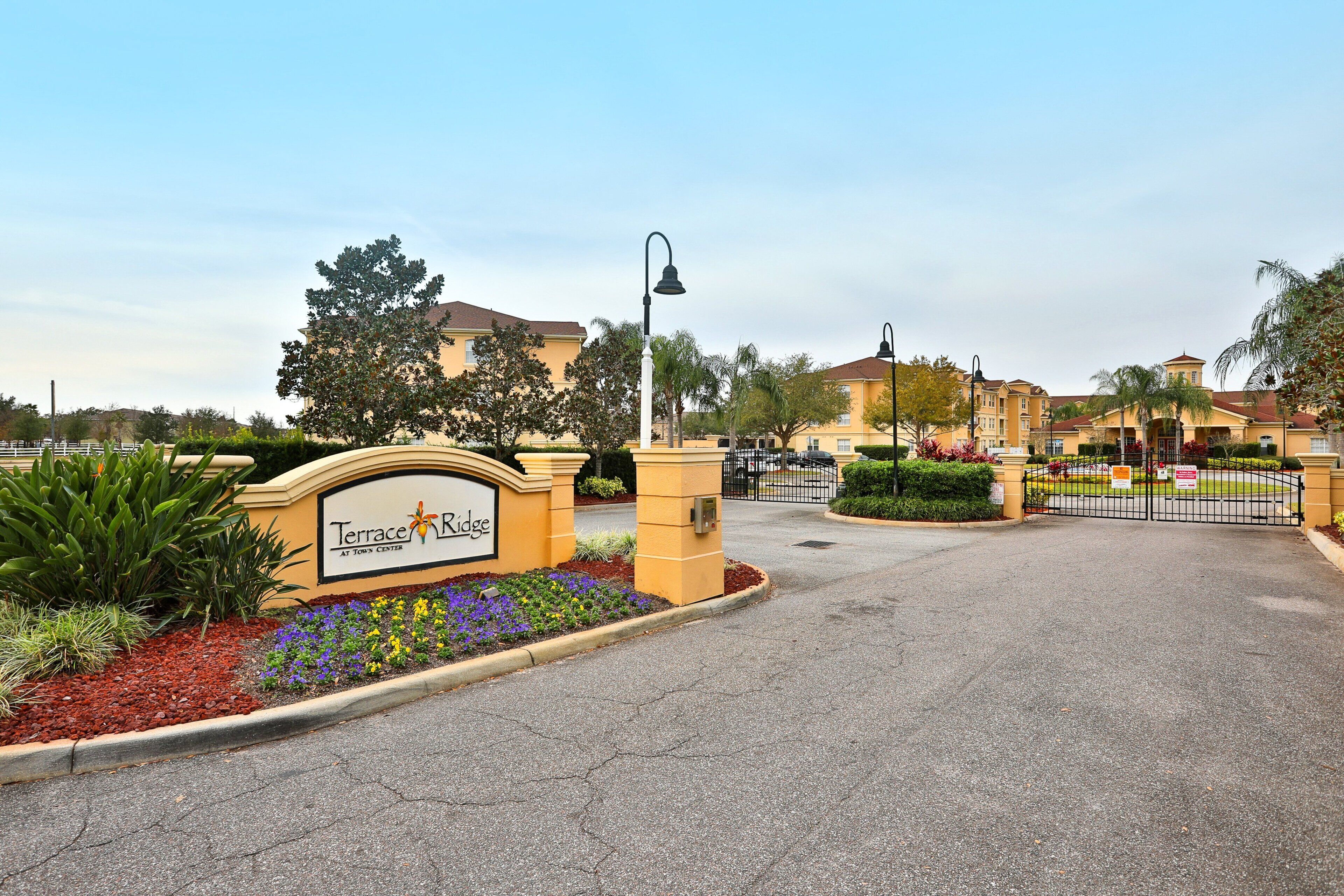 A gated entrance with a sign for Terrace Ridge, surrounded by landscaped areas with various plants and a clear sky.